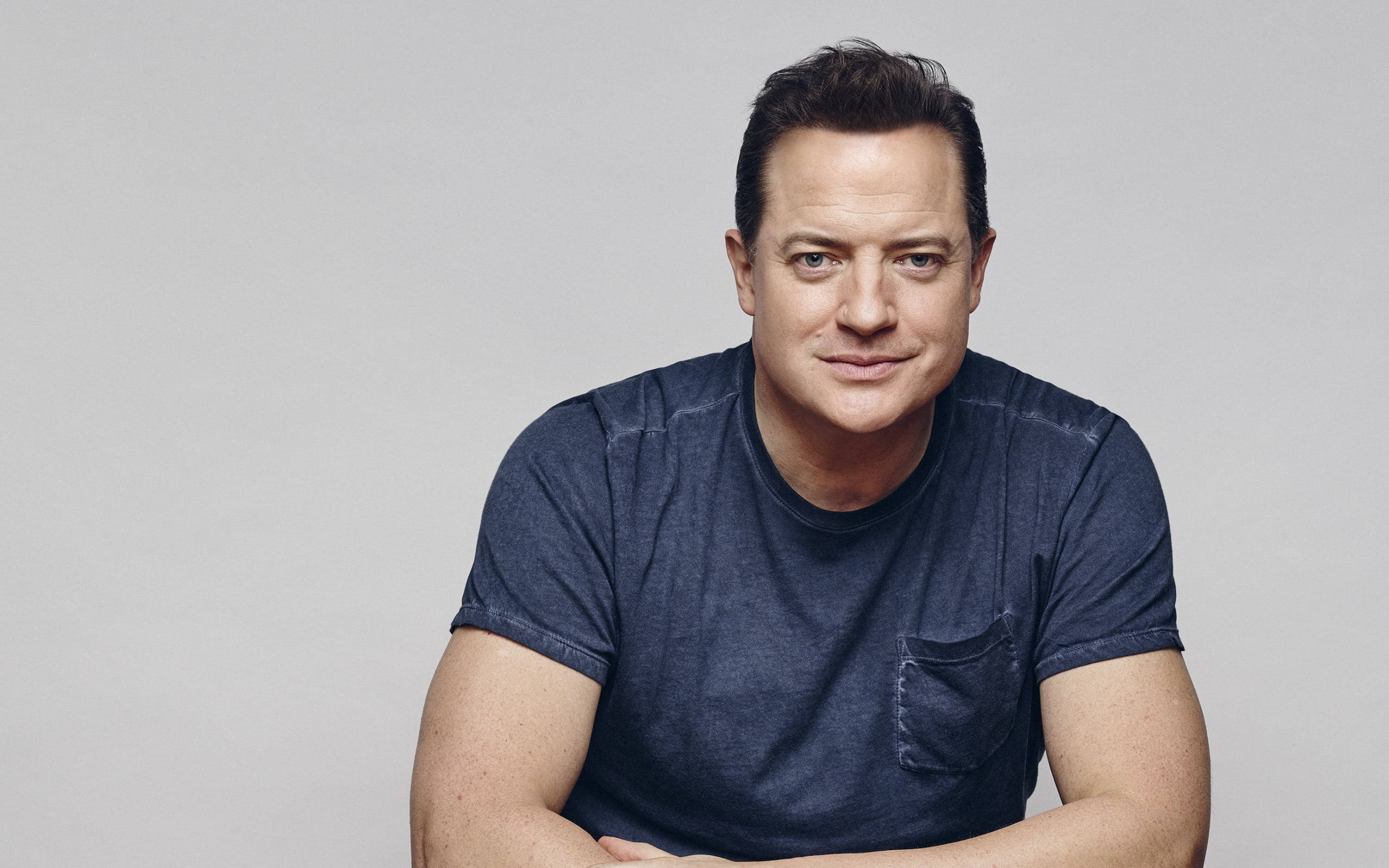 Brendan Fraser, dark blue t-shirt, plain gray studio background, 2K Desktop Wallpaper