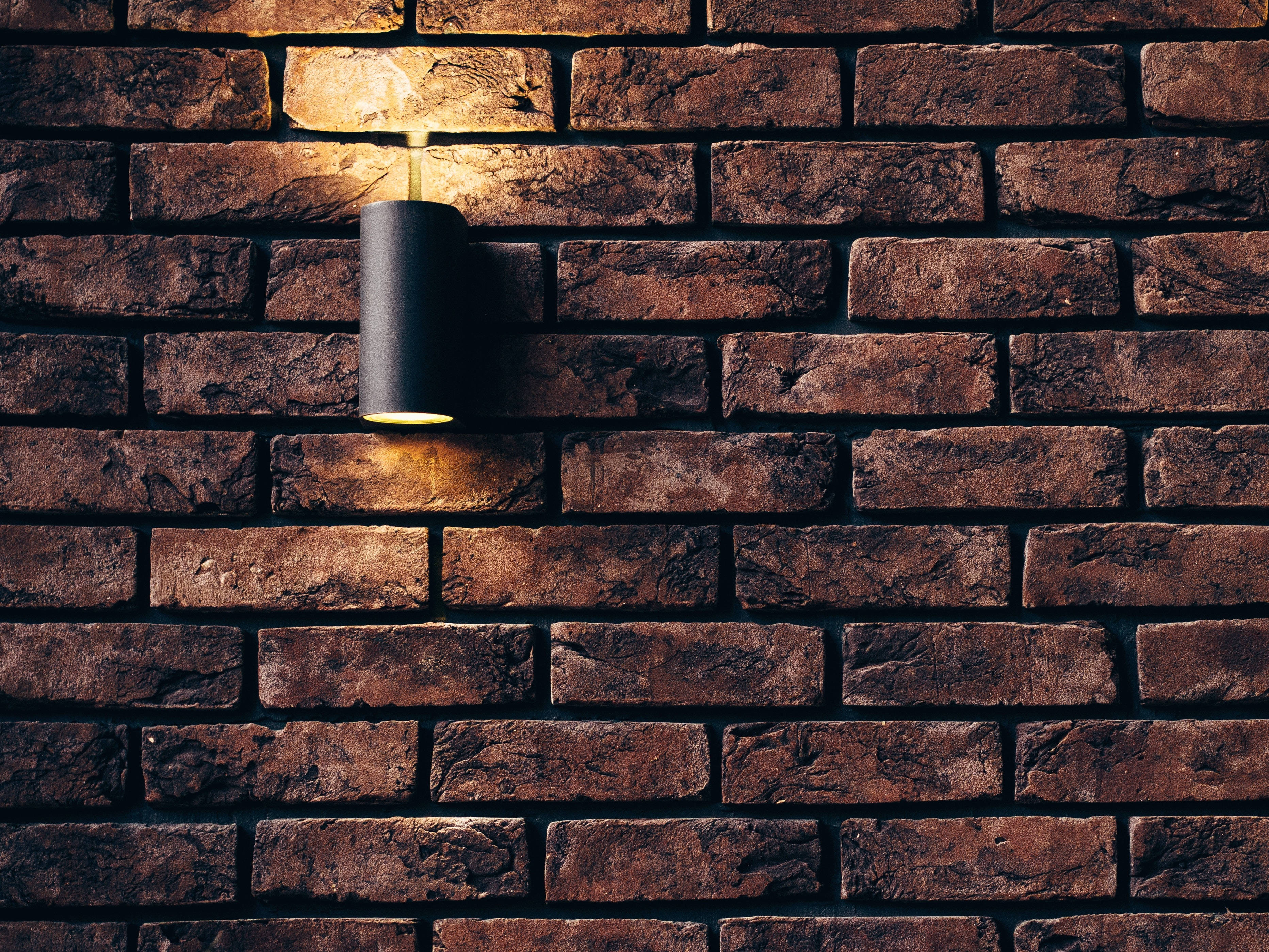 concrete texture tubular black sconce, warm golden light, textured rustic brick wall, 2K Desktop Wallpaper