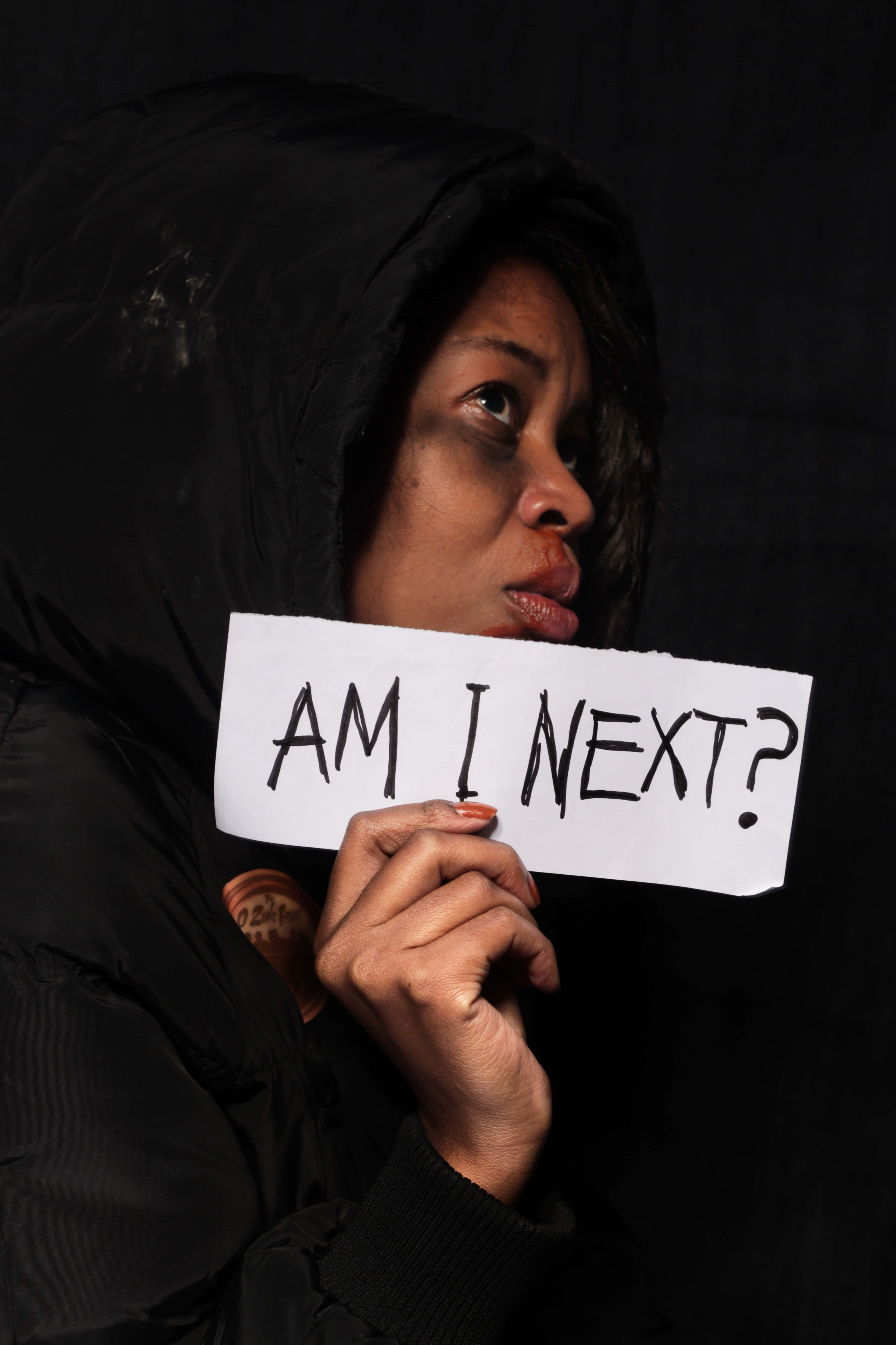 bruised girl am i next sign, black hooded jacket, sign reading AM I NEXT, 5K Phone Wallpaper