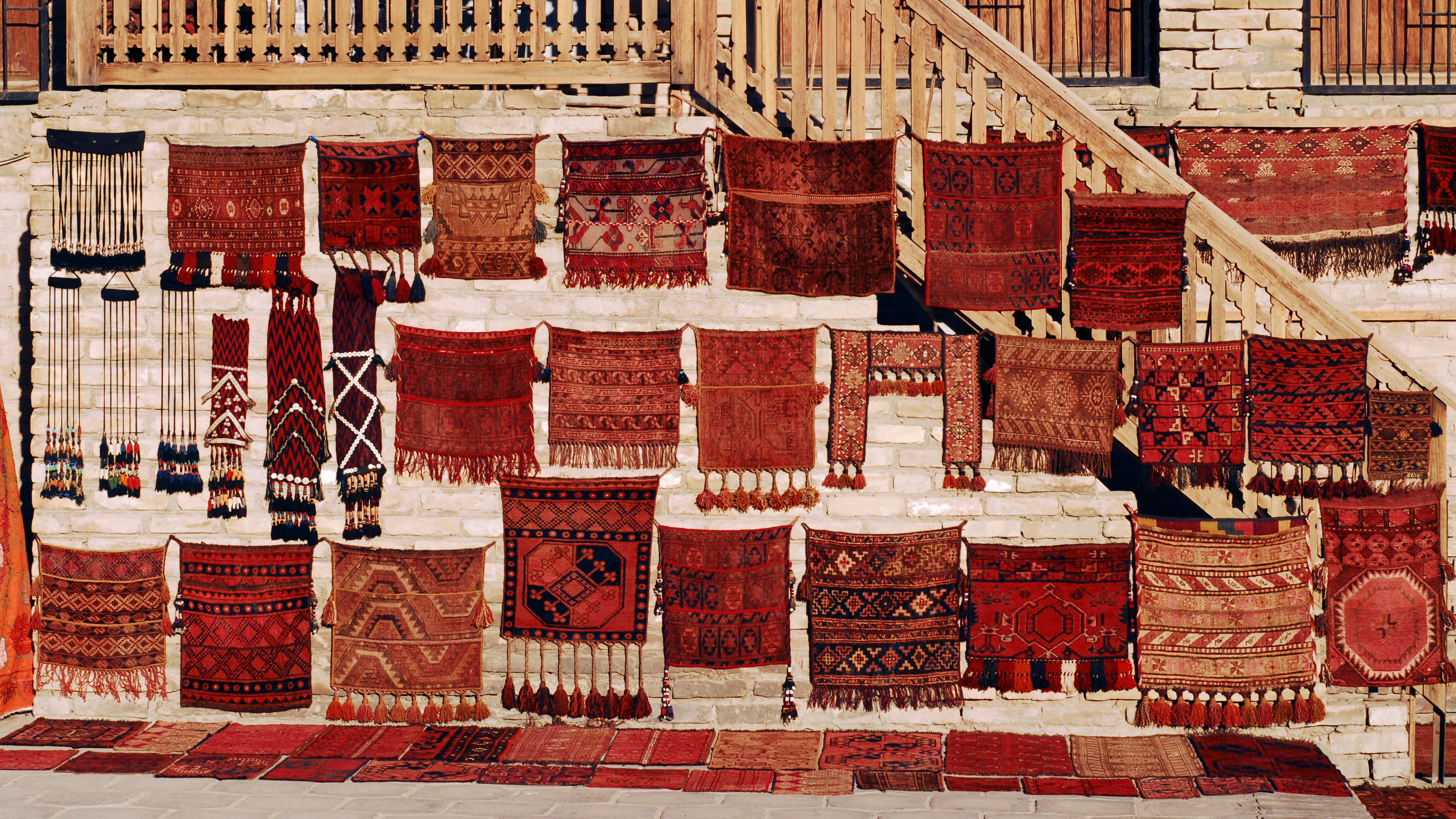 Bukhara, vibrant red patterned rugs, weathered stone wall, 4K Desktop Wallpaper