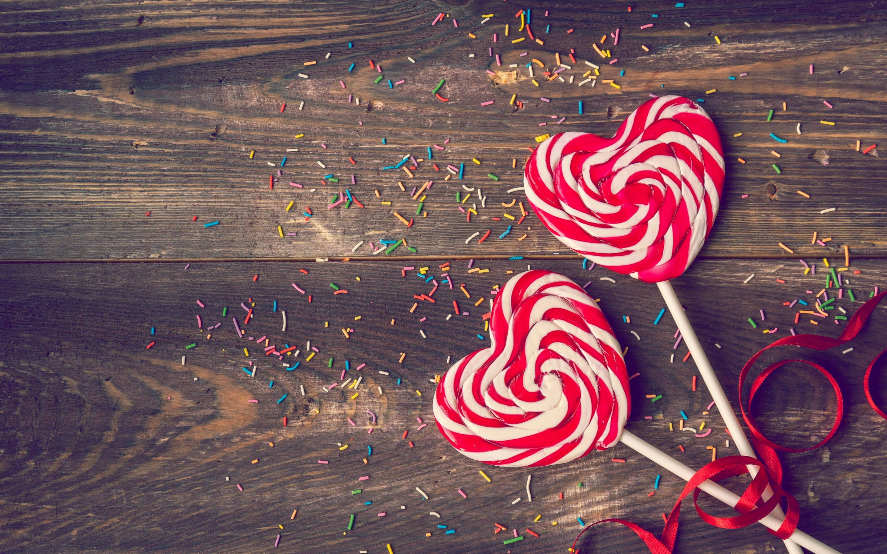 heart-shaped red and white swirled lollipops, colorful sprinkles, red ribbon, 2K Desktop Wallpaper