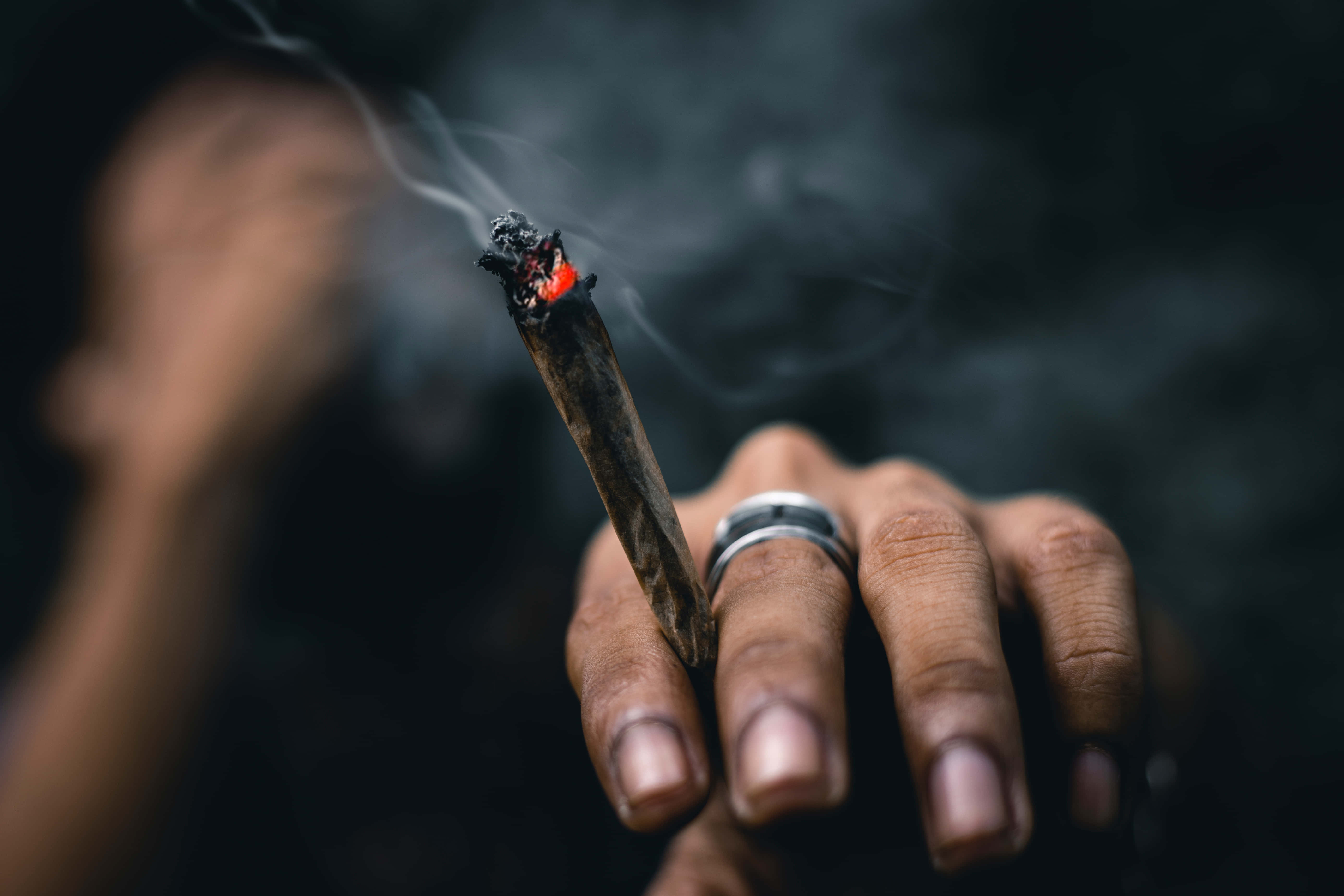 lit cannabis joint, smoke curling upward, dark blurred background, 5K Desktop Wallpaper