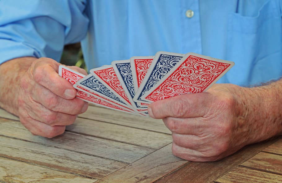 red and blue patterned playing cards, weathered wooden table, older person's hands, SD Desktop Wallpaper