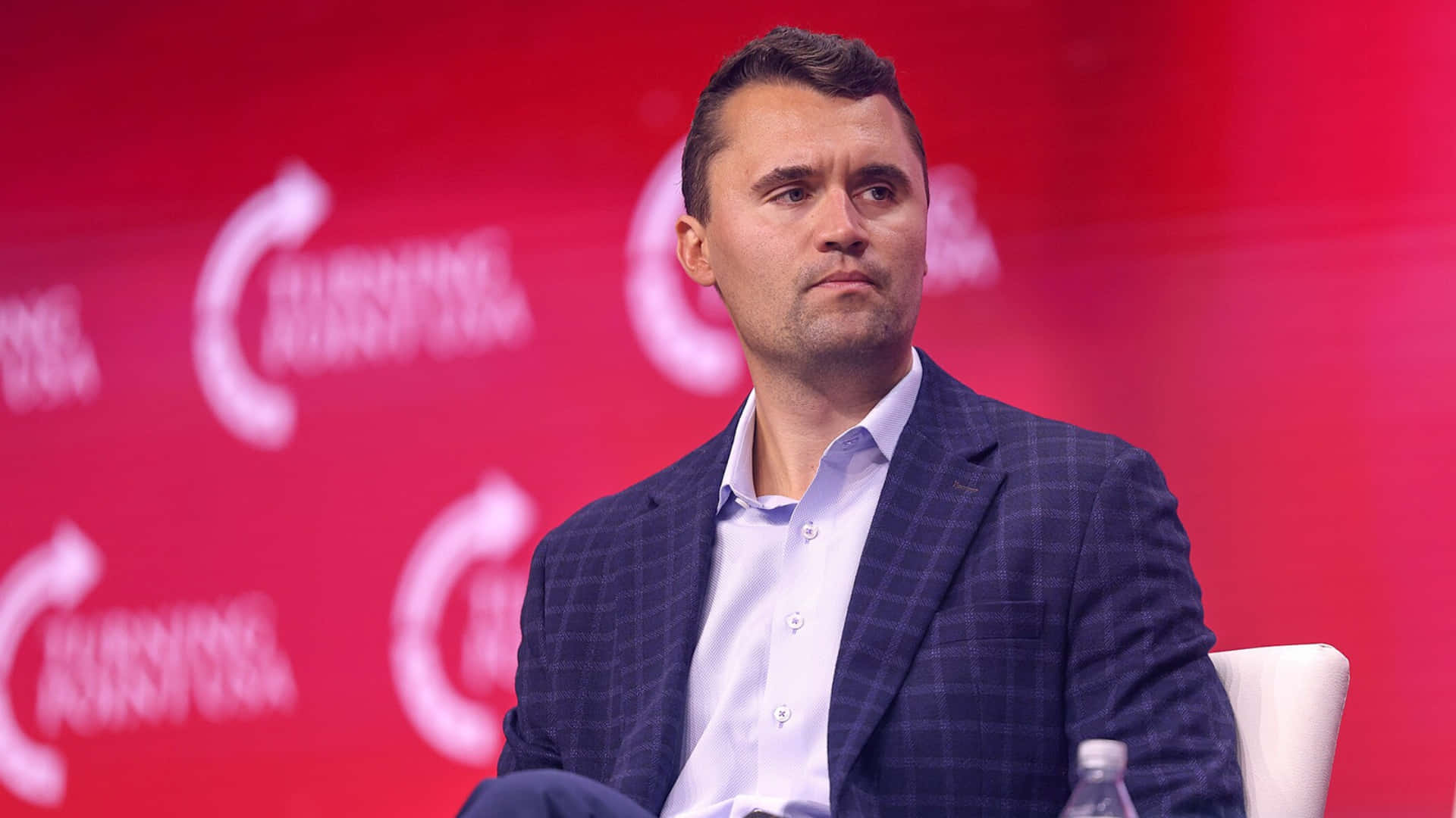 Charlie Kirk, blue checkered suit, vibrant red backdrop, Full HD Desktop Wallpaper