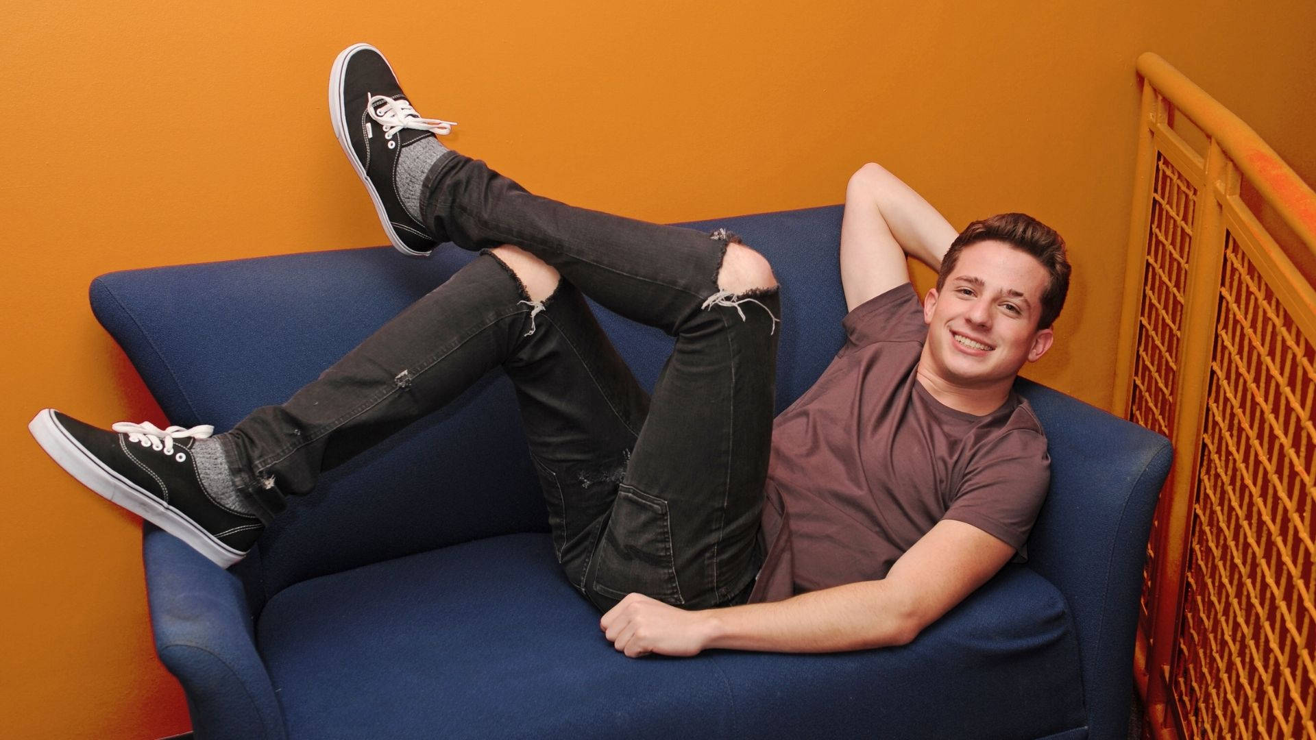 Charlie Puth, blue couch, vibrant orange wall, Full HD Desktop Wallpaper