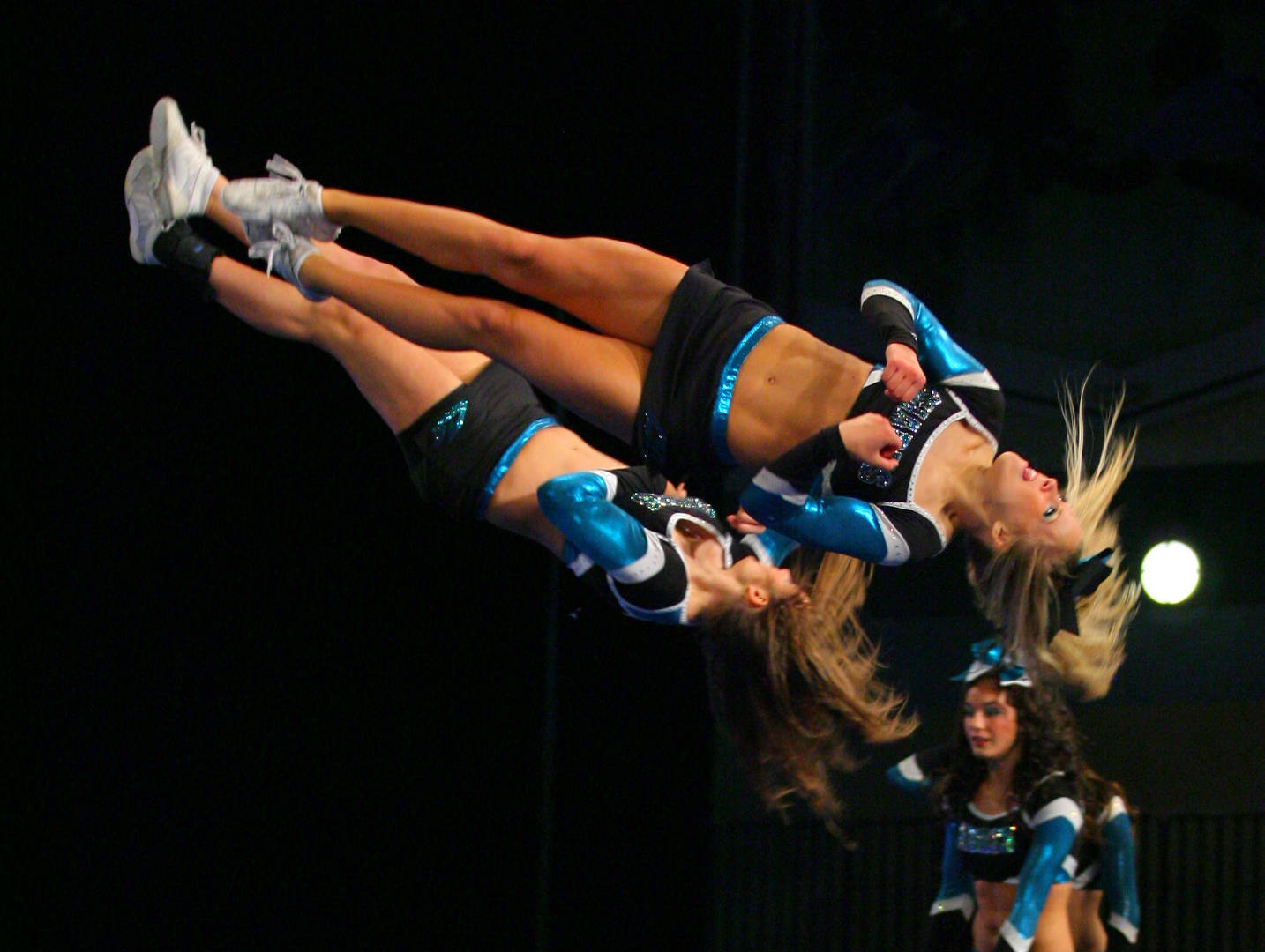 blue and black uniforms, dynamic mid-air stunt, dark stage backdrop, HD Desktop Wallpaper