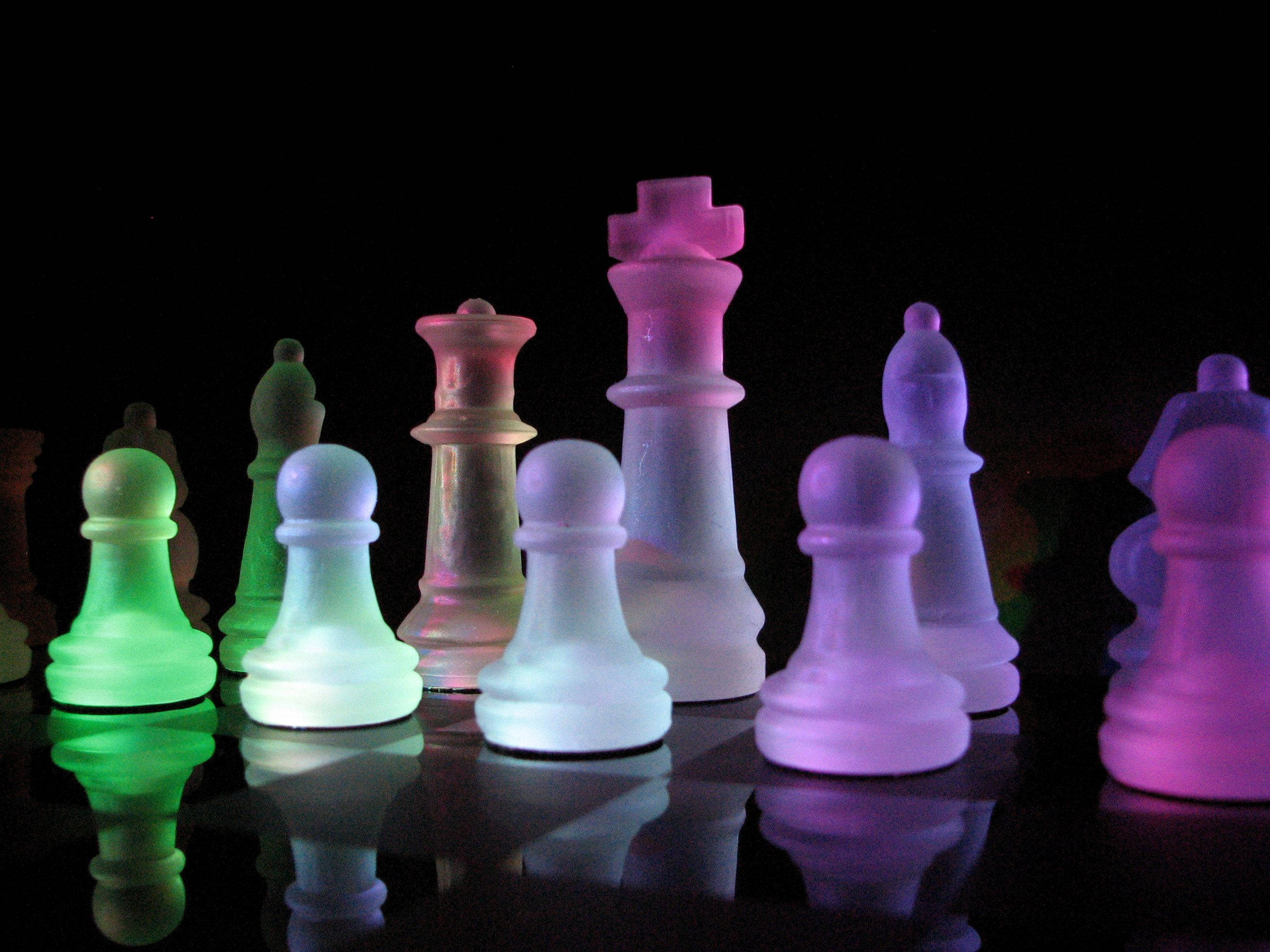 illuminated frosted chess pieces, vibrant neon hues, reflective surface, 2K Desktop Wallpaper