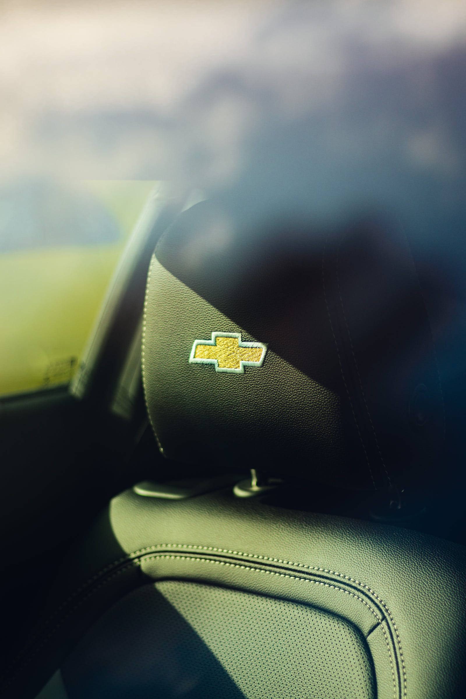 Chevrolet logo, black leather car headrest, sunlight, Full HD Phone Wallpaper
