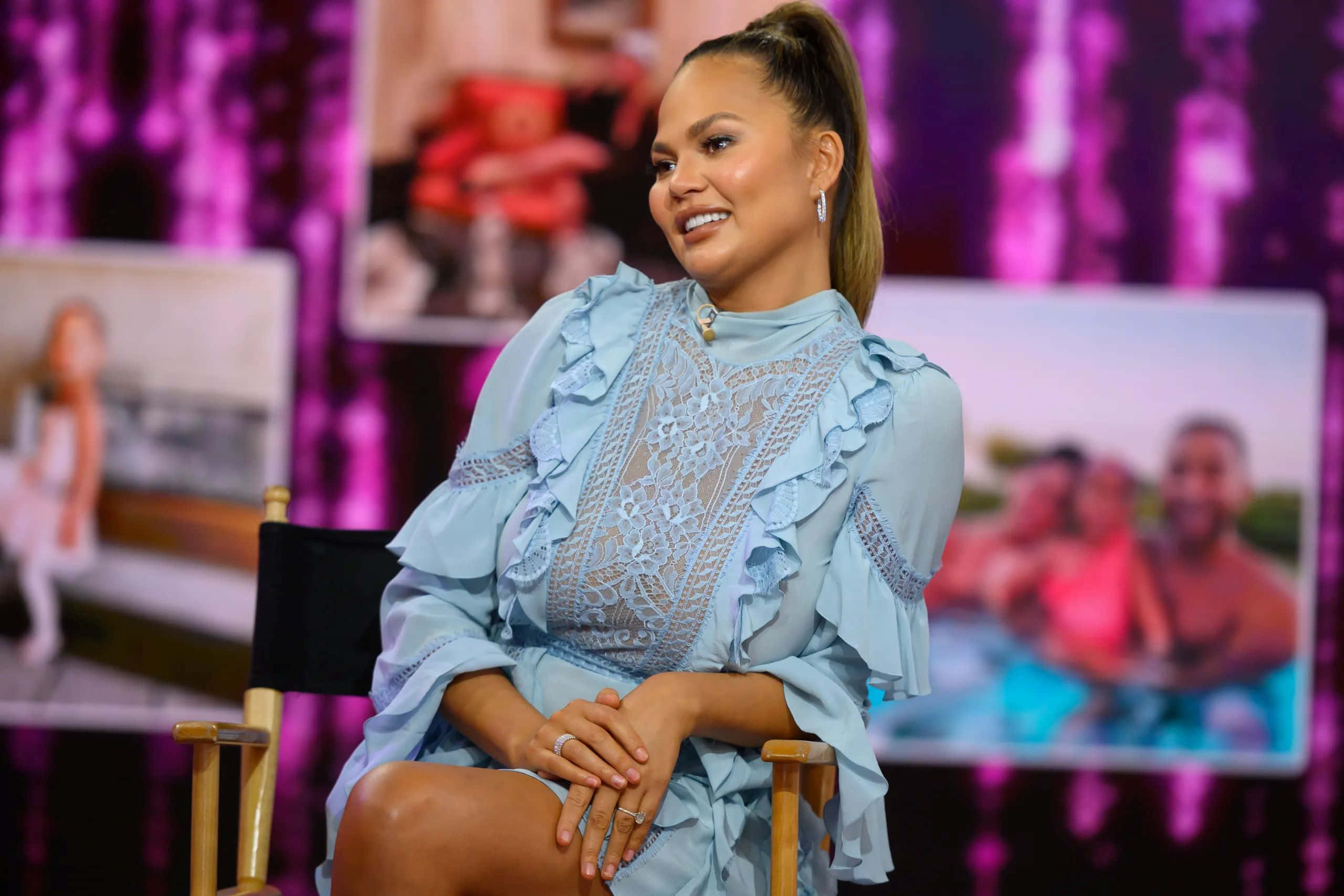 Chrissy Teigen, director's chair, vibrant purple backdrop, 2K Desktop Wallpaper