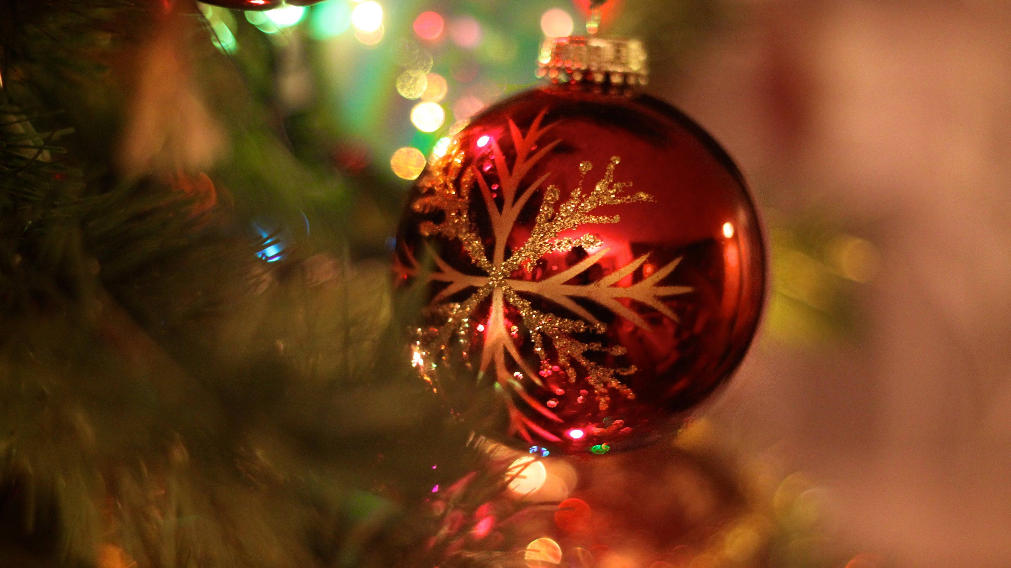 glossy red Christmas ornament, glittering gold snowflake design, blurred green tree branches, 4K Desktop Wallpaper