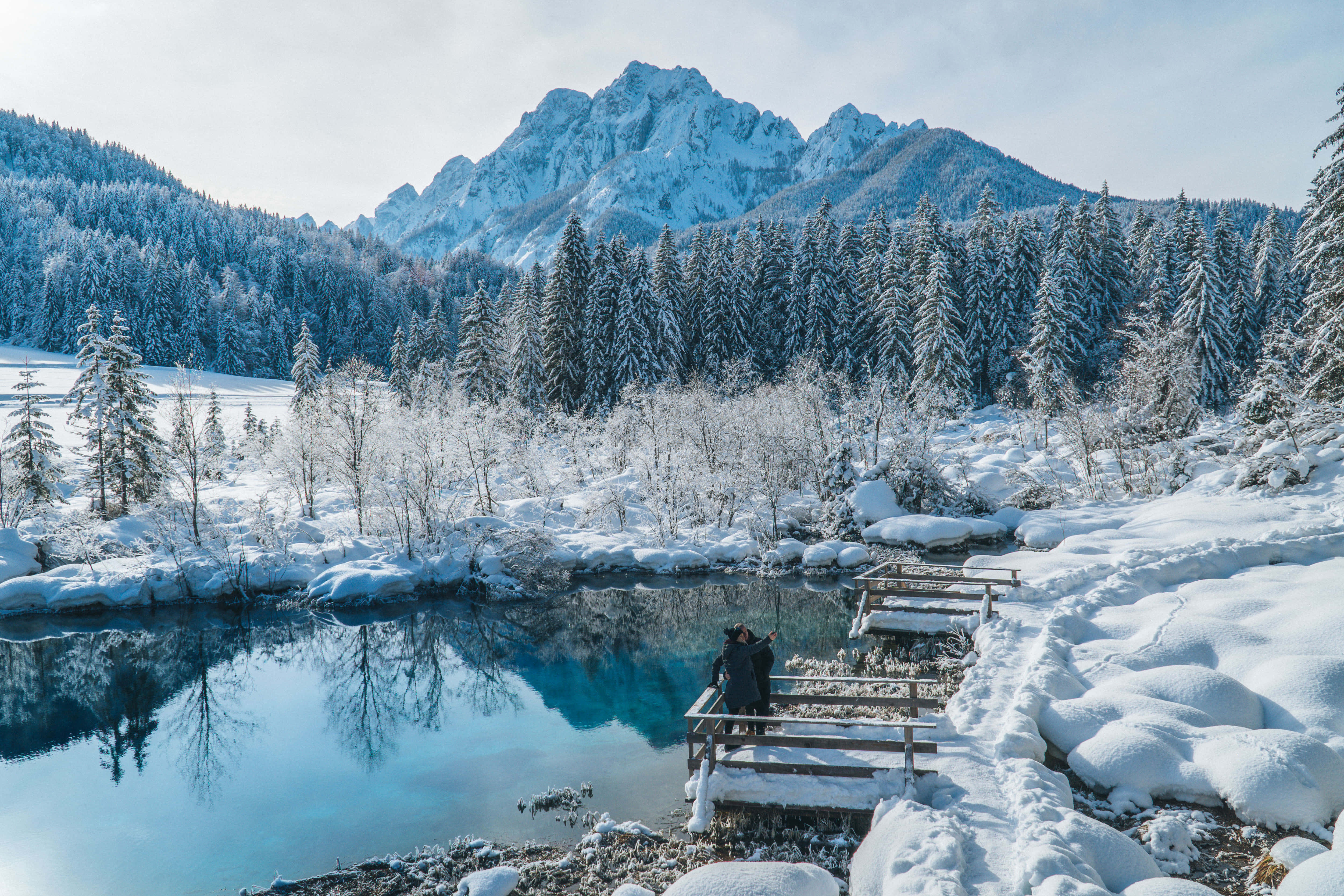 Christmas Winter Wonderland, snow-dusted wooden bridge, vivid blue lake, 4K Desktop Wallpaper