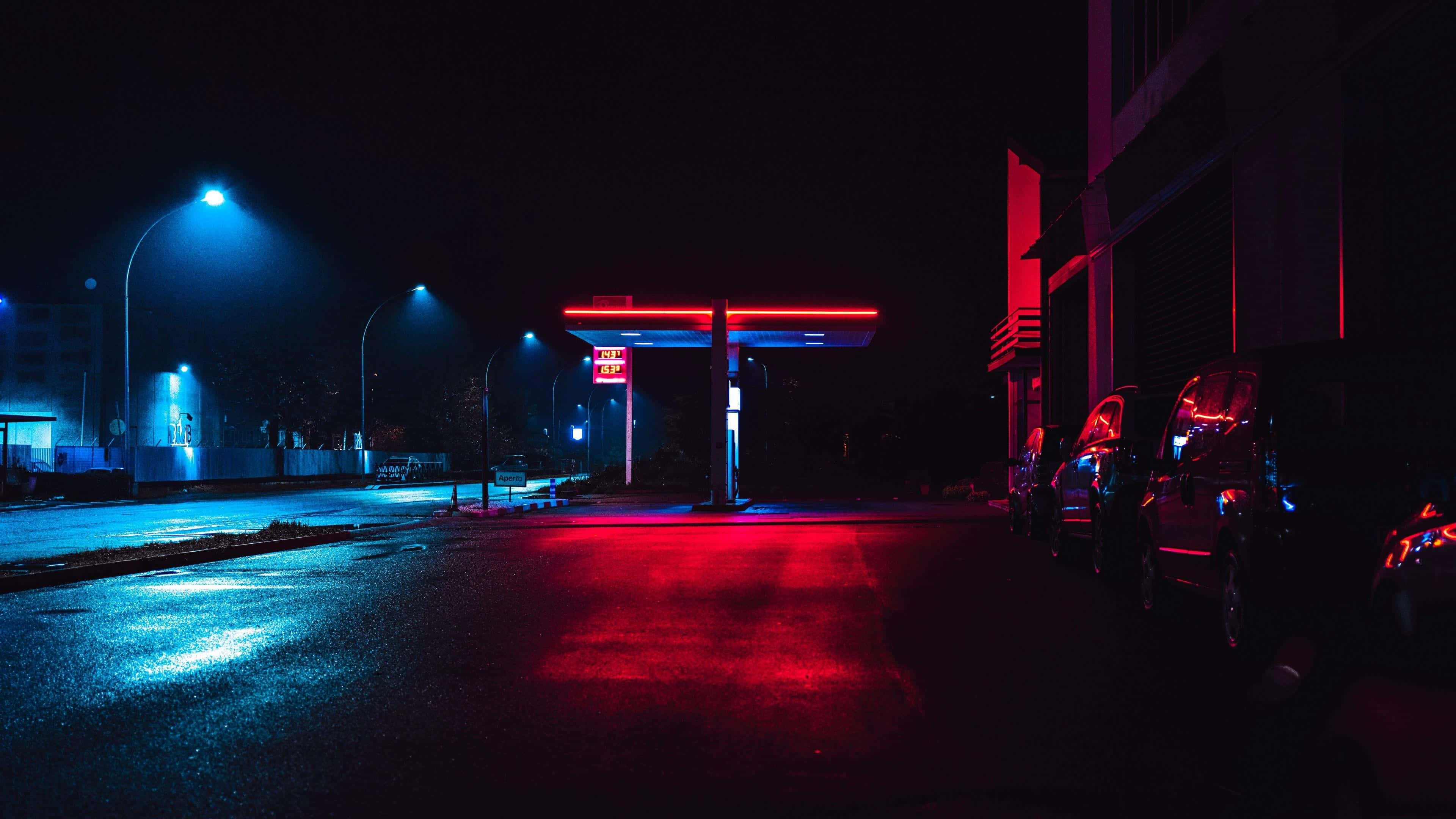 neon-lit gas station, red and blue lights, wet pavement, 4K Desktop Wallpaper