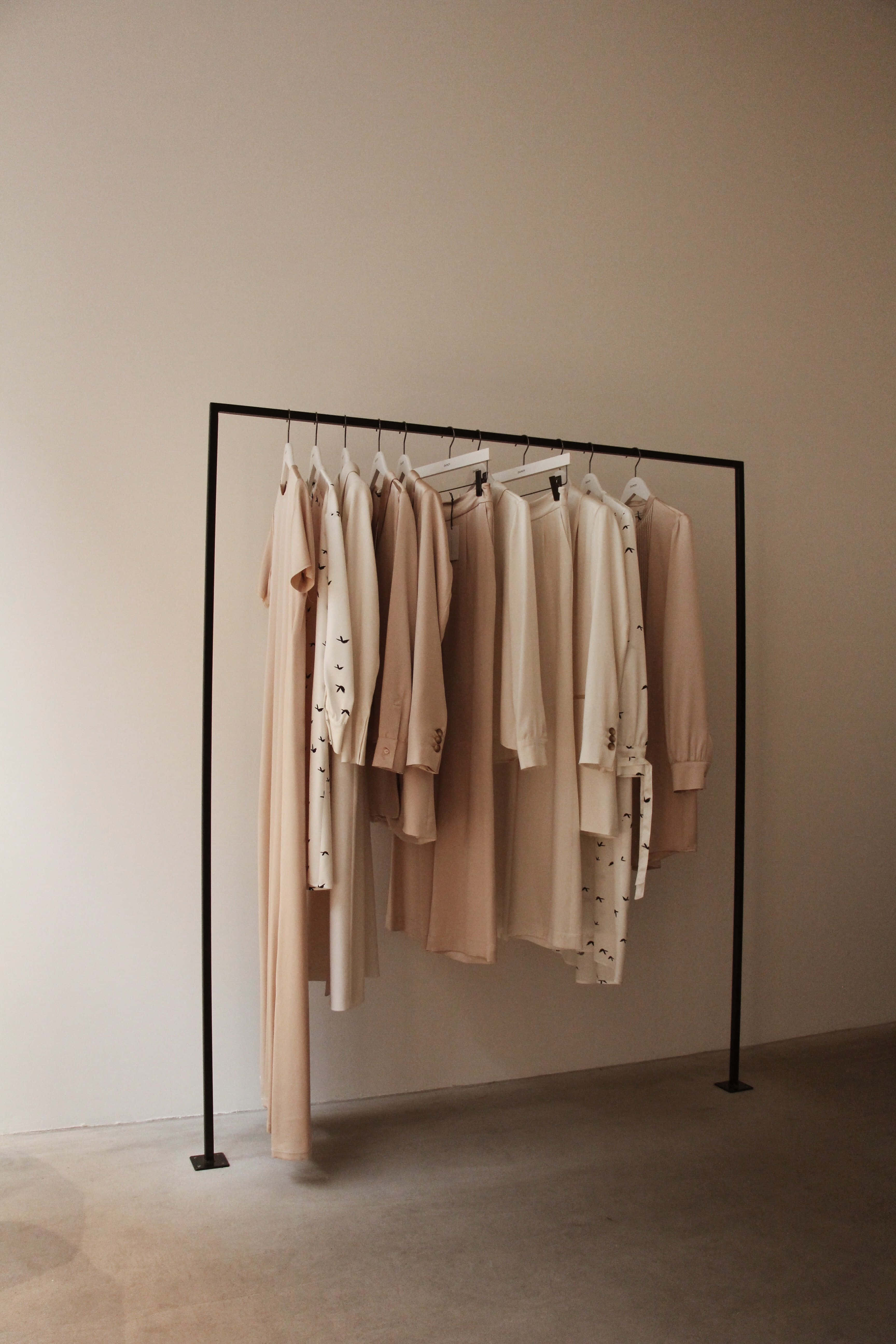 minimalist clothing rack, soft beige and cream garments, neutral wall, 5K Phone Wallpaper