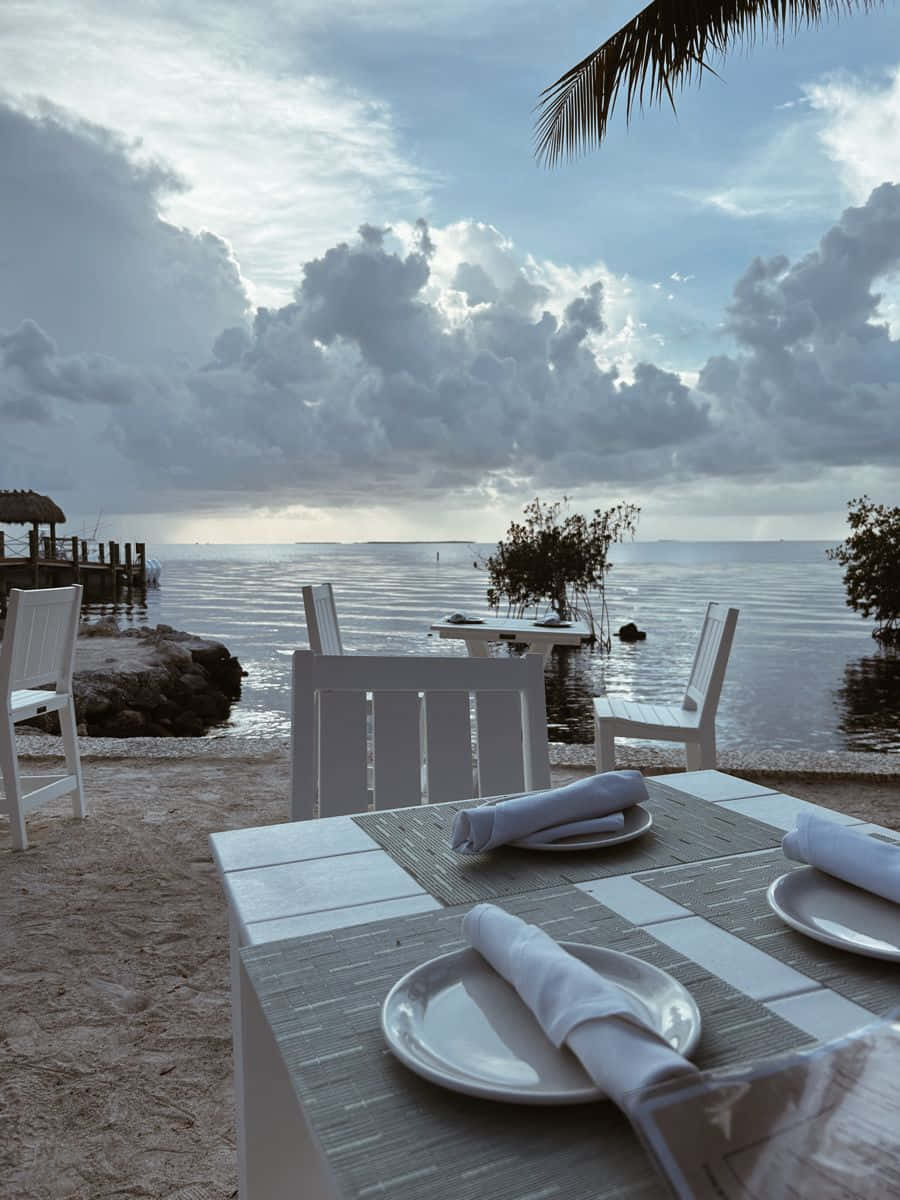 Coastal Dining Experience, beachside table, cloudy sky, SD Phone Wallpaper