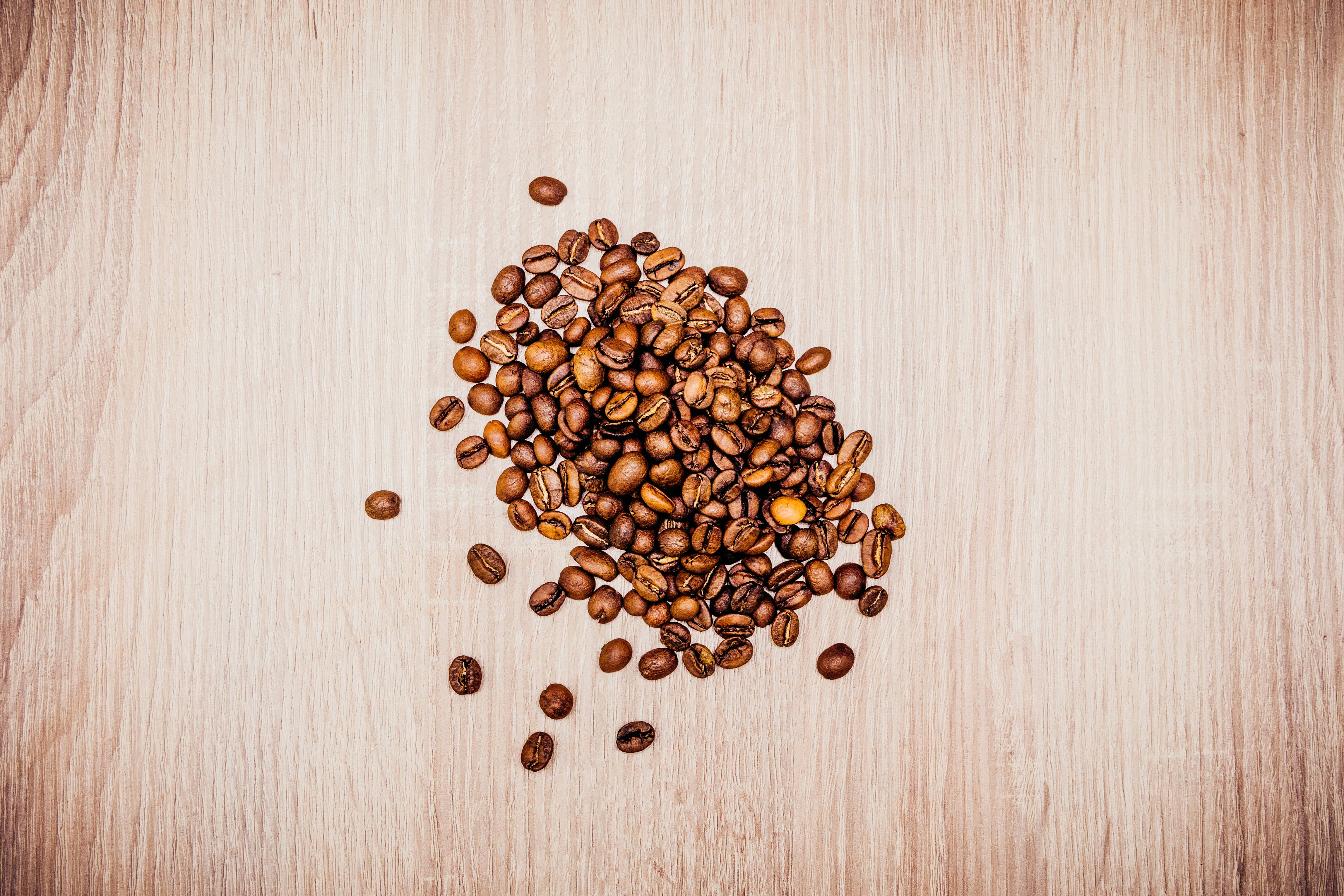 roasted coffee beans, light wooden surface, visible grain, 4K Desktop Wallpaper