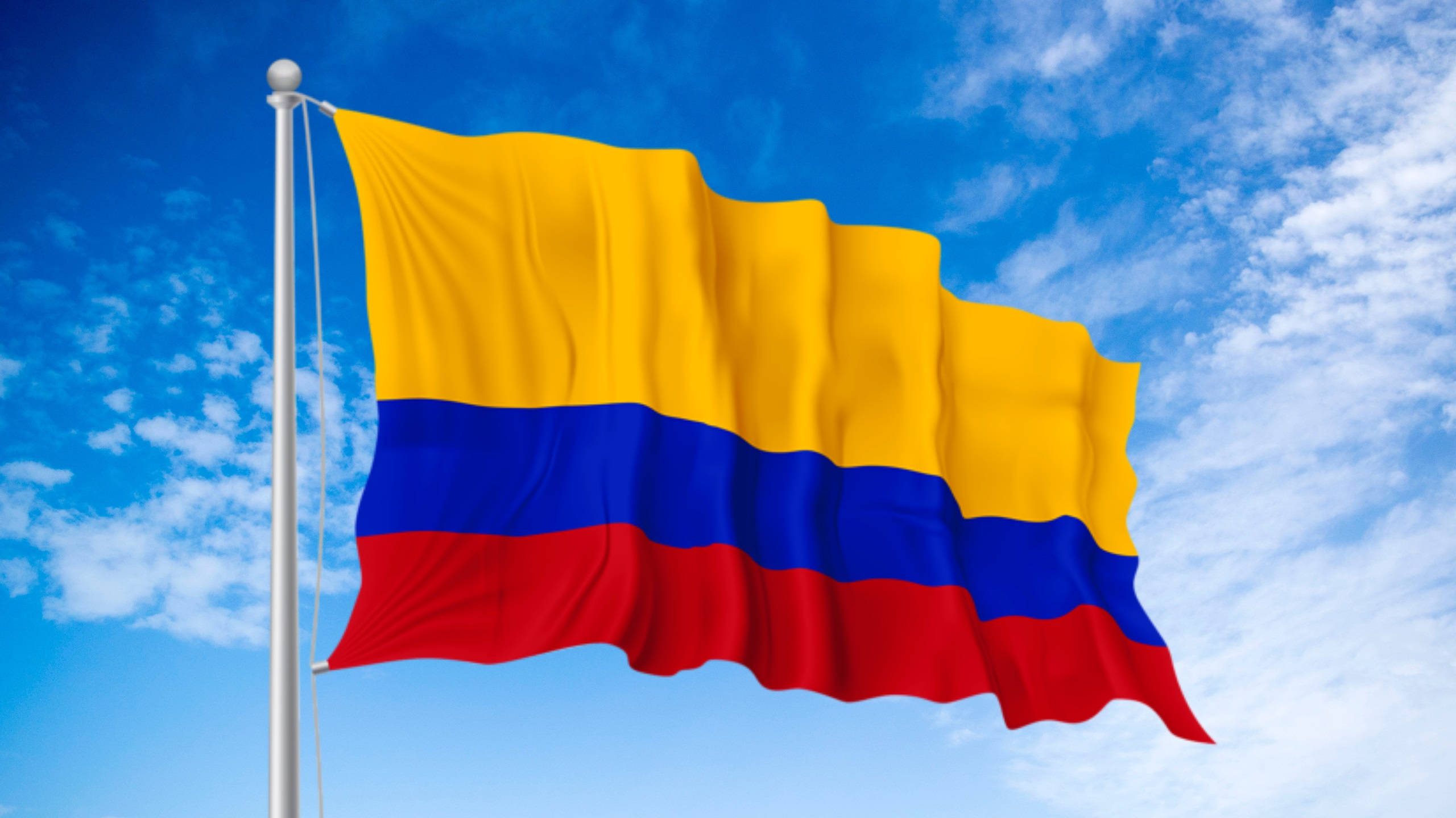 Colombia flag, bright blue sky, scattered white clouds, 2K Desktop Wallpaper