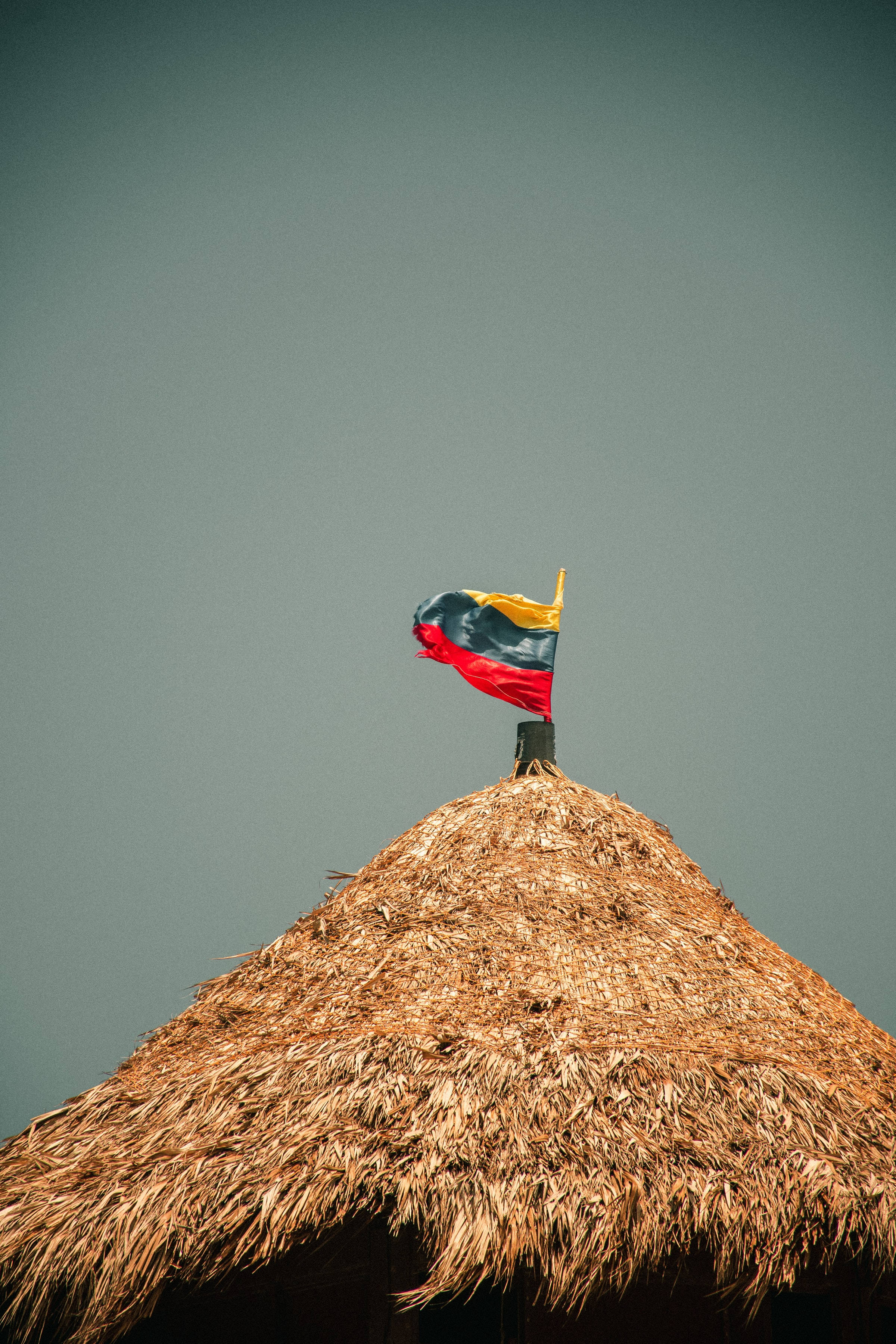 Colombia flag, rustic thatched roof, muted gray sky, 2K Phone Wallpaper