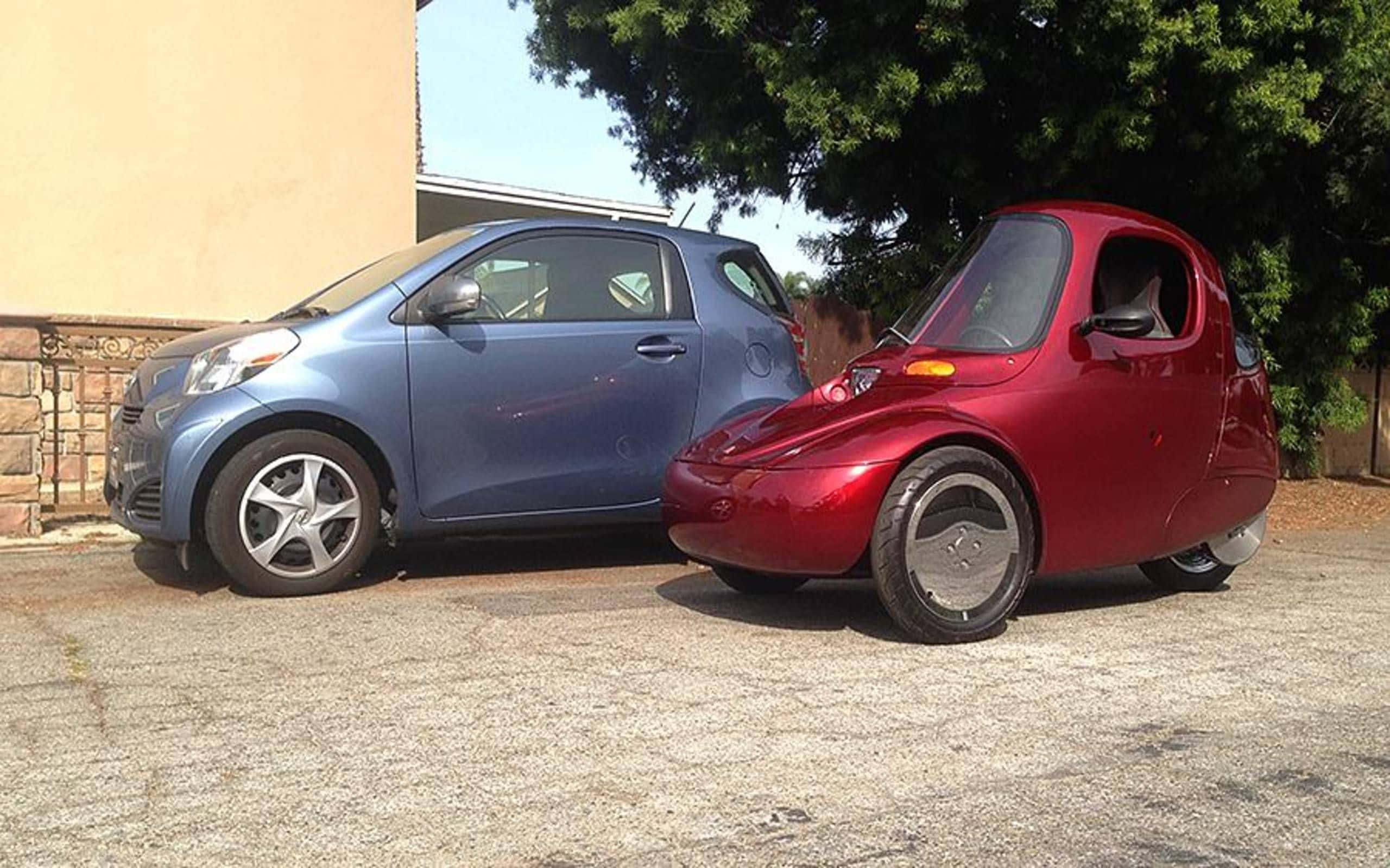 shiny red three-wheeled microcar, blue compact car, sunlit concrete driveway, 2K Desktop Wallpaper