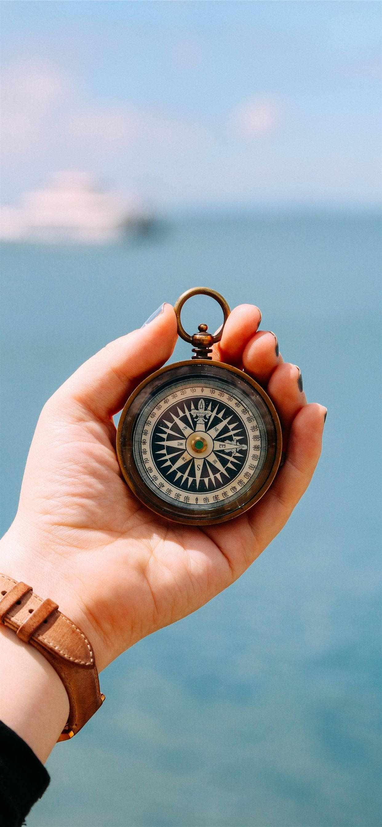 vintage brass compass, hand, blurred ocean backdrop, 2K Phone Wallpaper