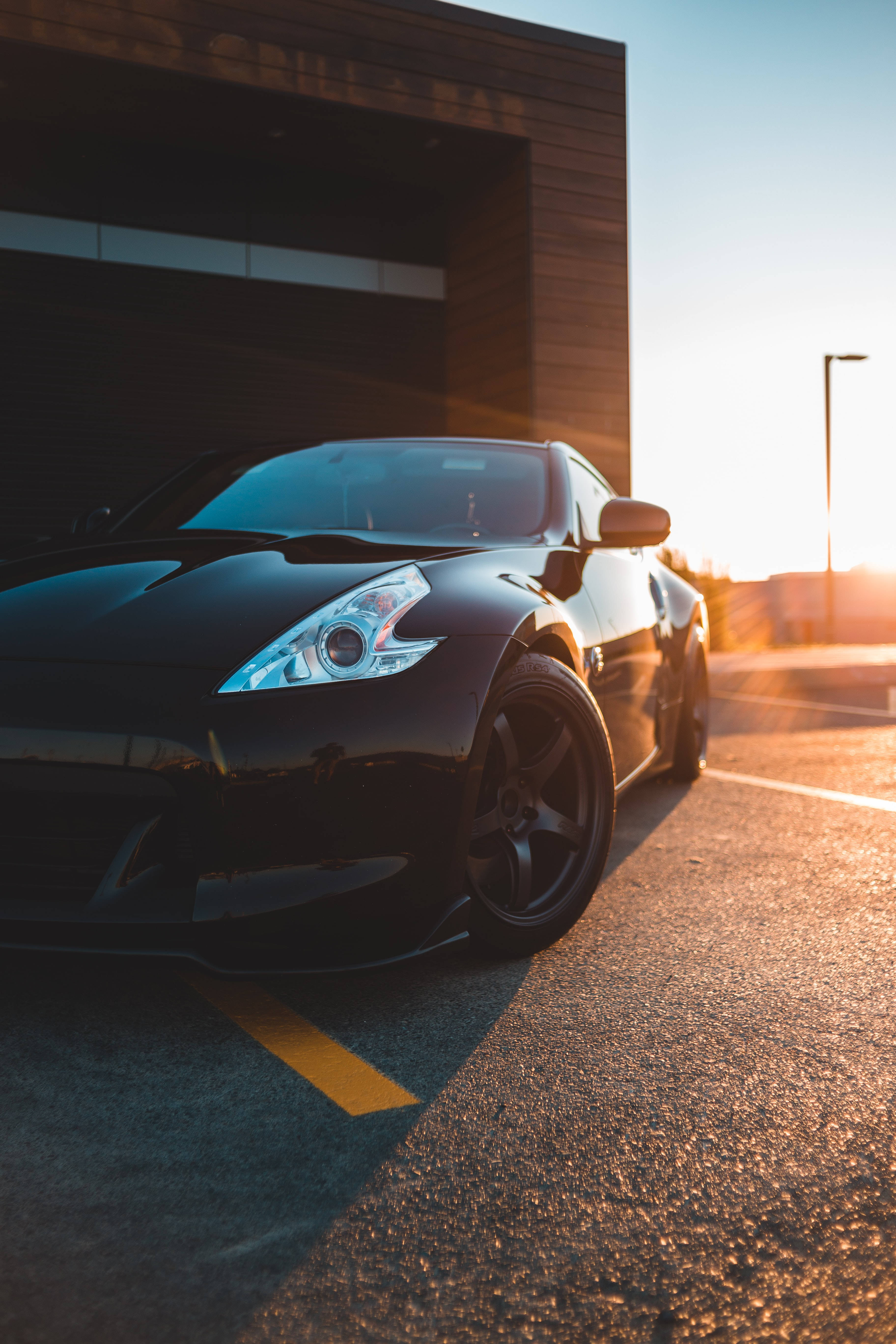 shiny black sports car, golden sunset light, modern wooden building, 5K Phone Wallpaper