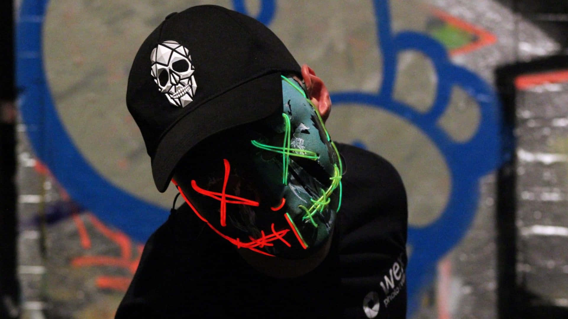 black cap with skull logo, glowing red and green LED mask, graffiti-covered wall, Full HD Desktop Wallpaper