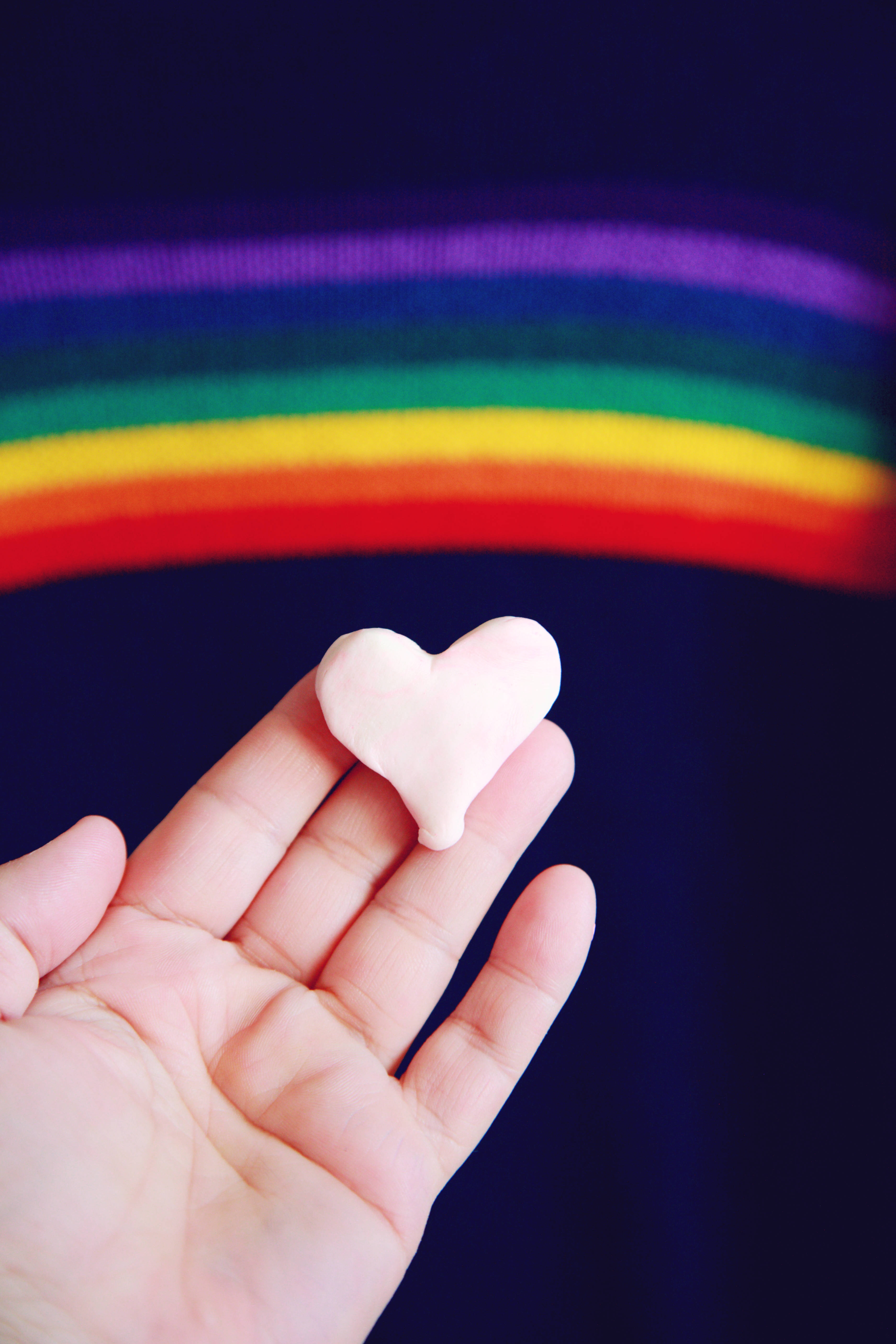 soft pink heart-shaped object, rainbow-striped fabric backdrop, hand, 5K Phone Wallpaper