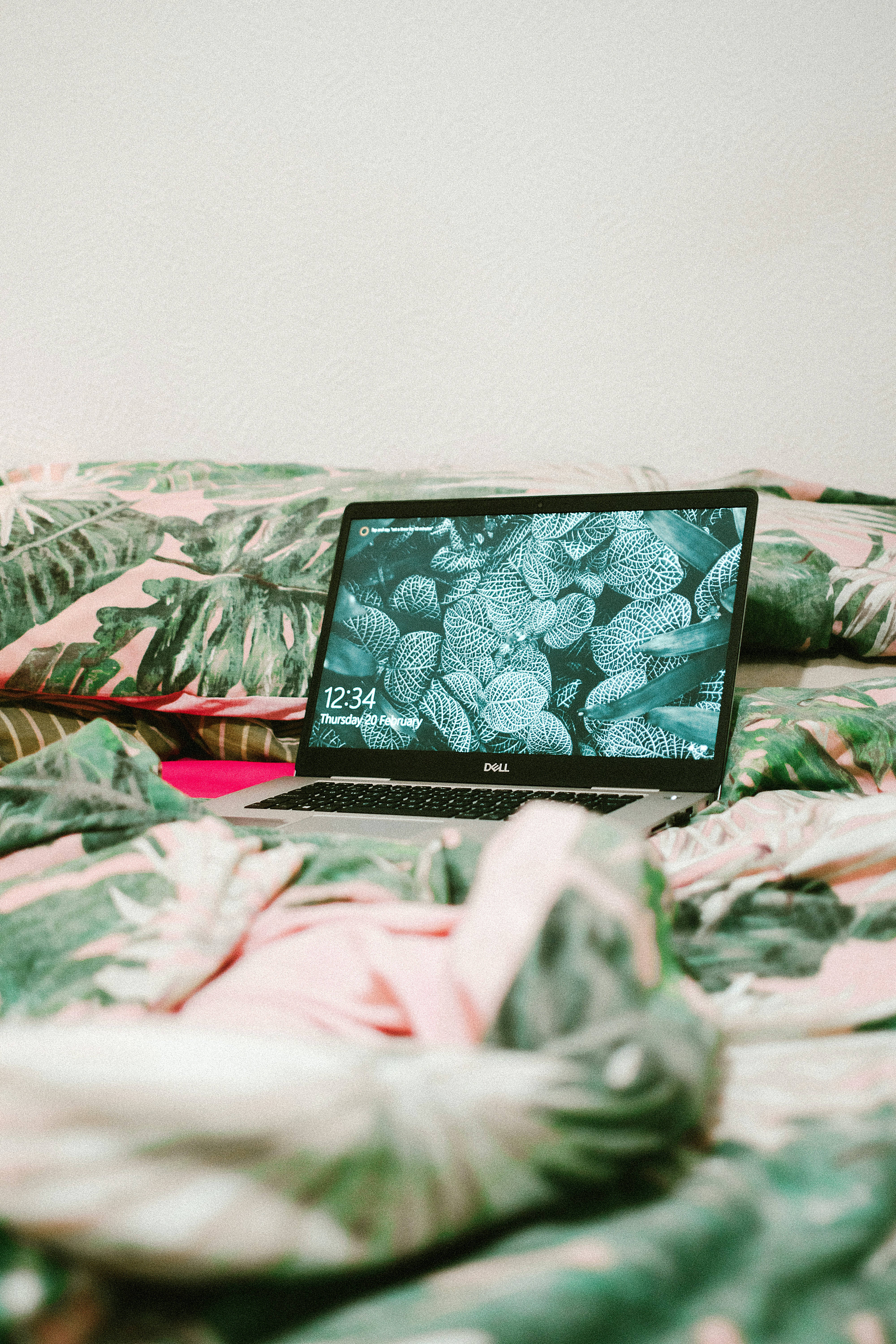 silver laptop, pink and green leaf-patterned bedspread, plain white wall, 5K Phone Wallpaper