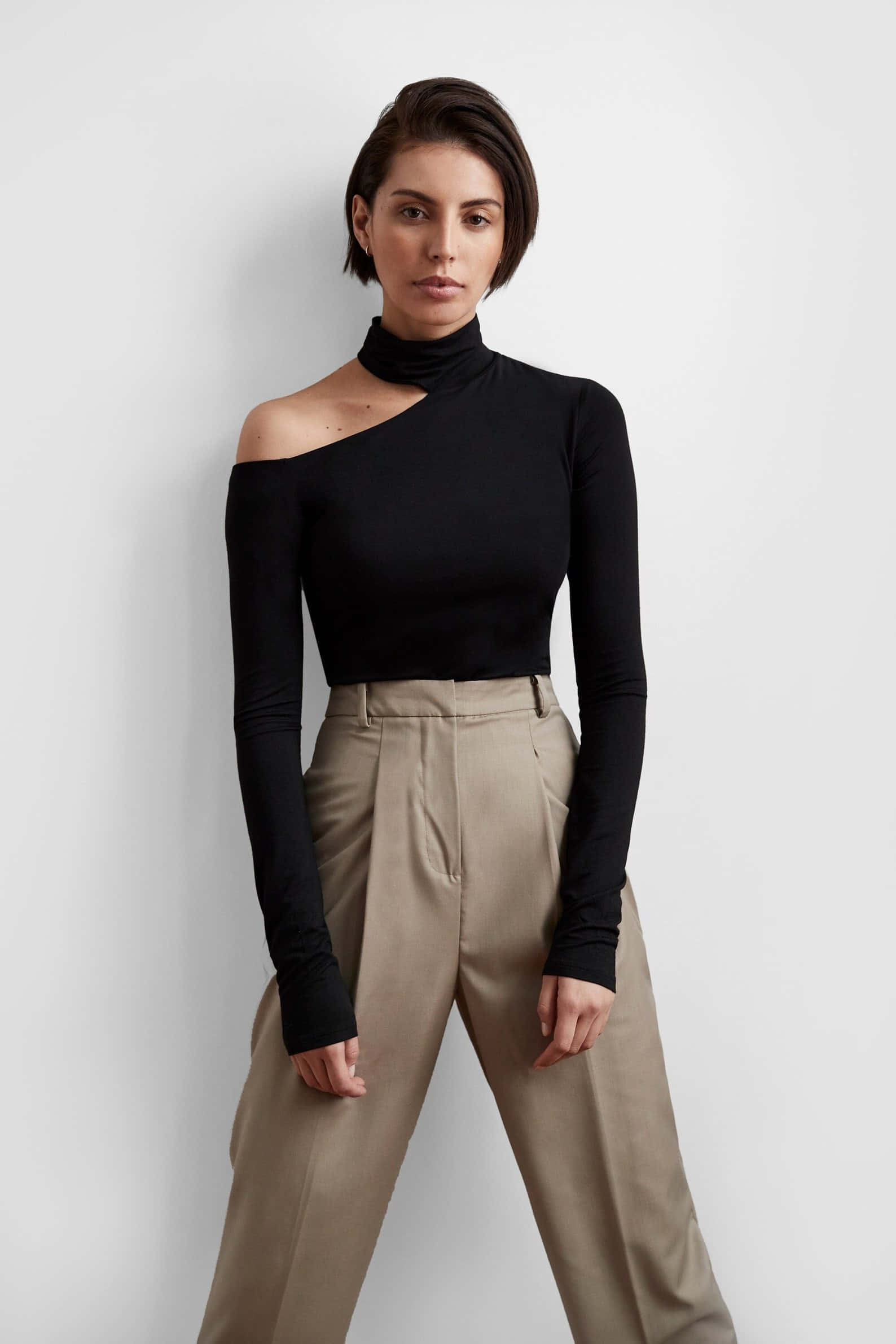 black one-shoulder turtleneck, beige high-waisted trousers, short dark hair, Full HD Phone Wallpaper