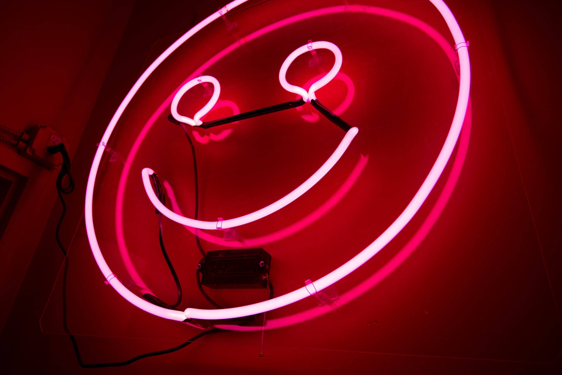 Steady Neon Smile, glowing pink neon smiley face sign, warm red light, Full HD Desktop Wallpaper