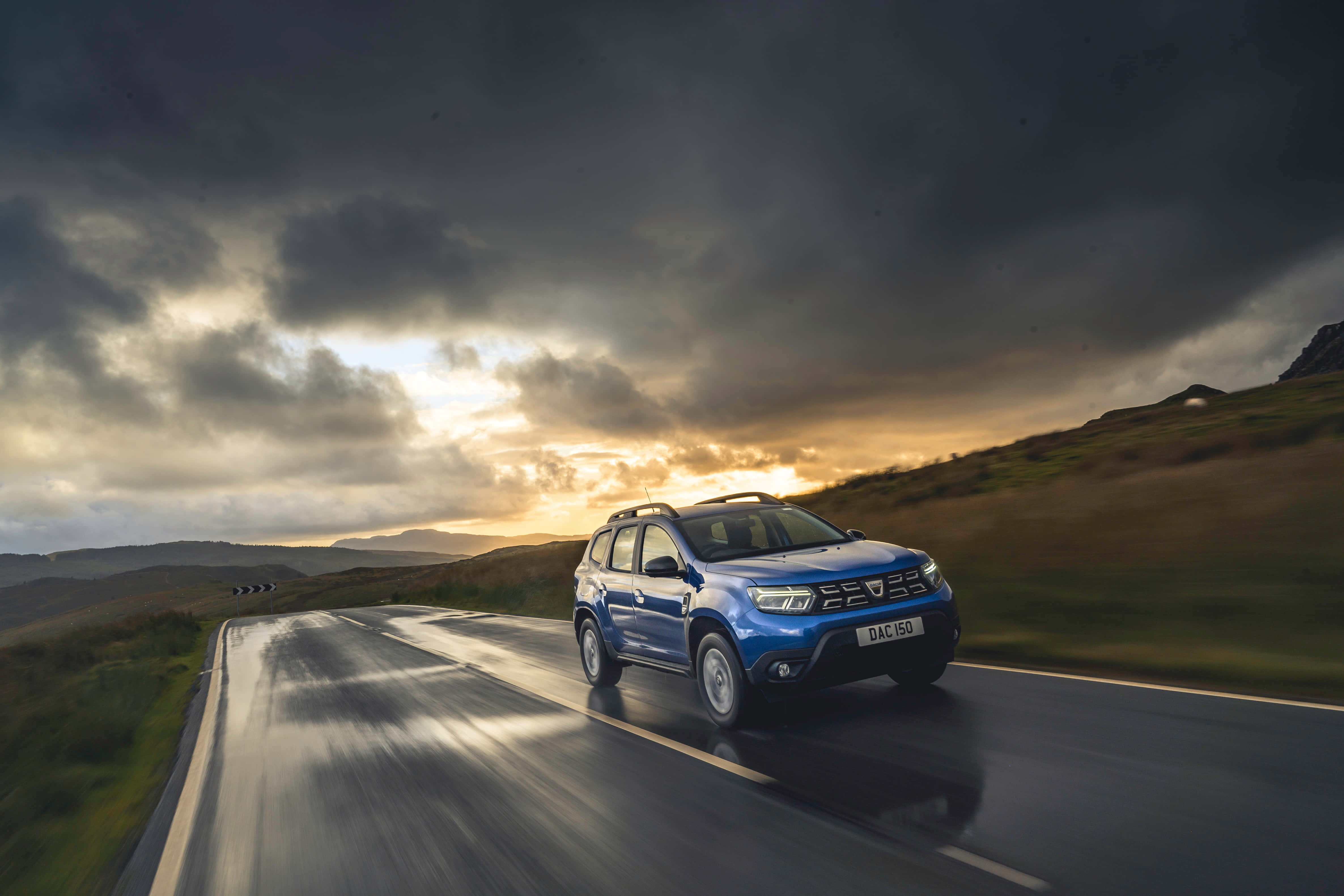 blue Dacia Duster, wet winding road, dramatic cloudy sunset sky, 4K Desktop Wallpaper