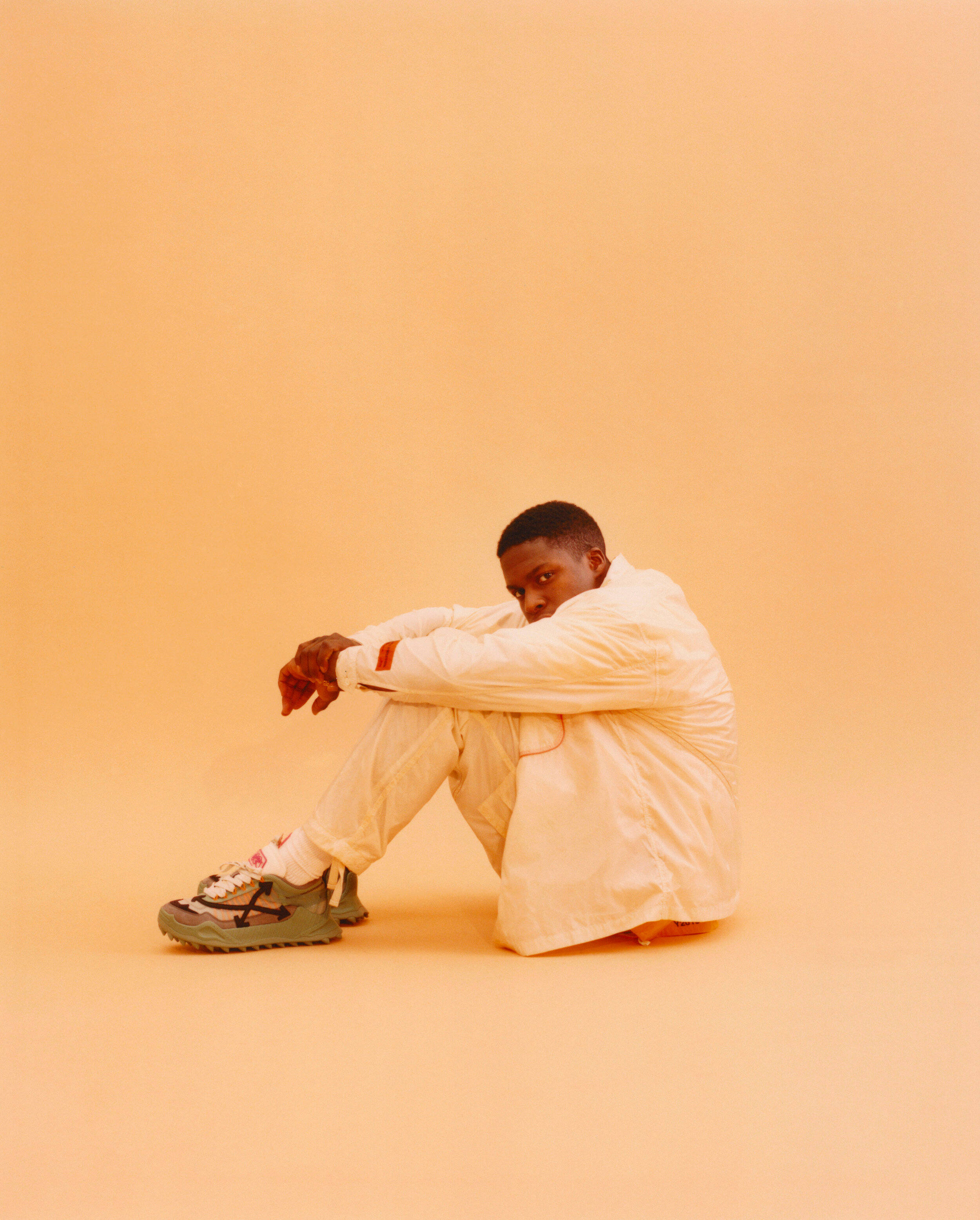 Daniel Caesar, white outfit, warm peach floor, 2K Phone Wallpaper