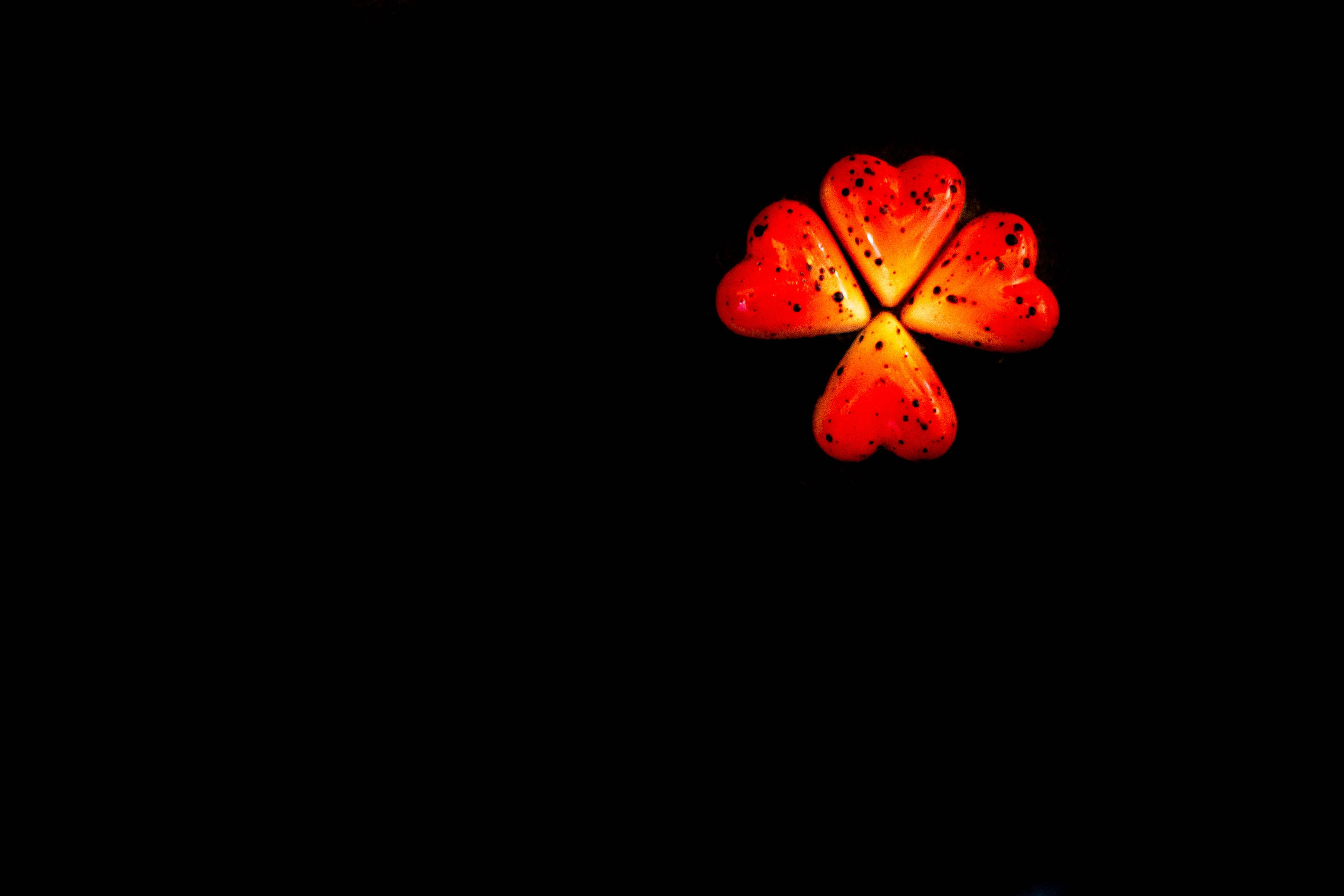 four clover leaf shaped dark heart, glossy red heart-shaped candies, black speckles, 2K Desktop Wallpaper