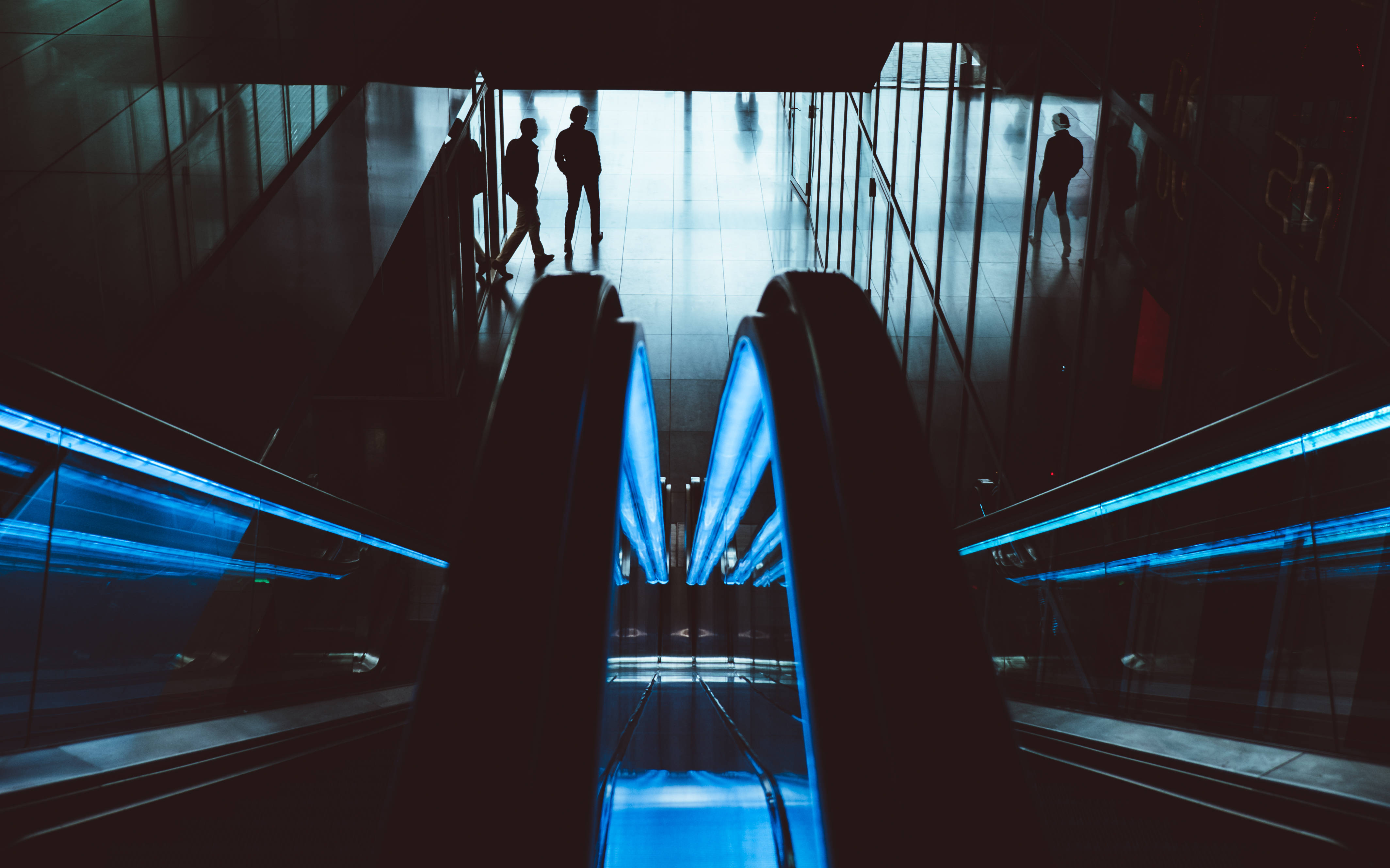 Dark Neon iPhone, glowing blue escalators, modern transit hub, 4K Desktop Wallpaper
