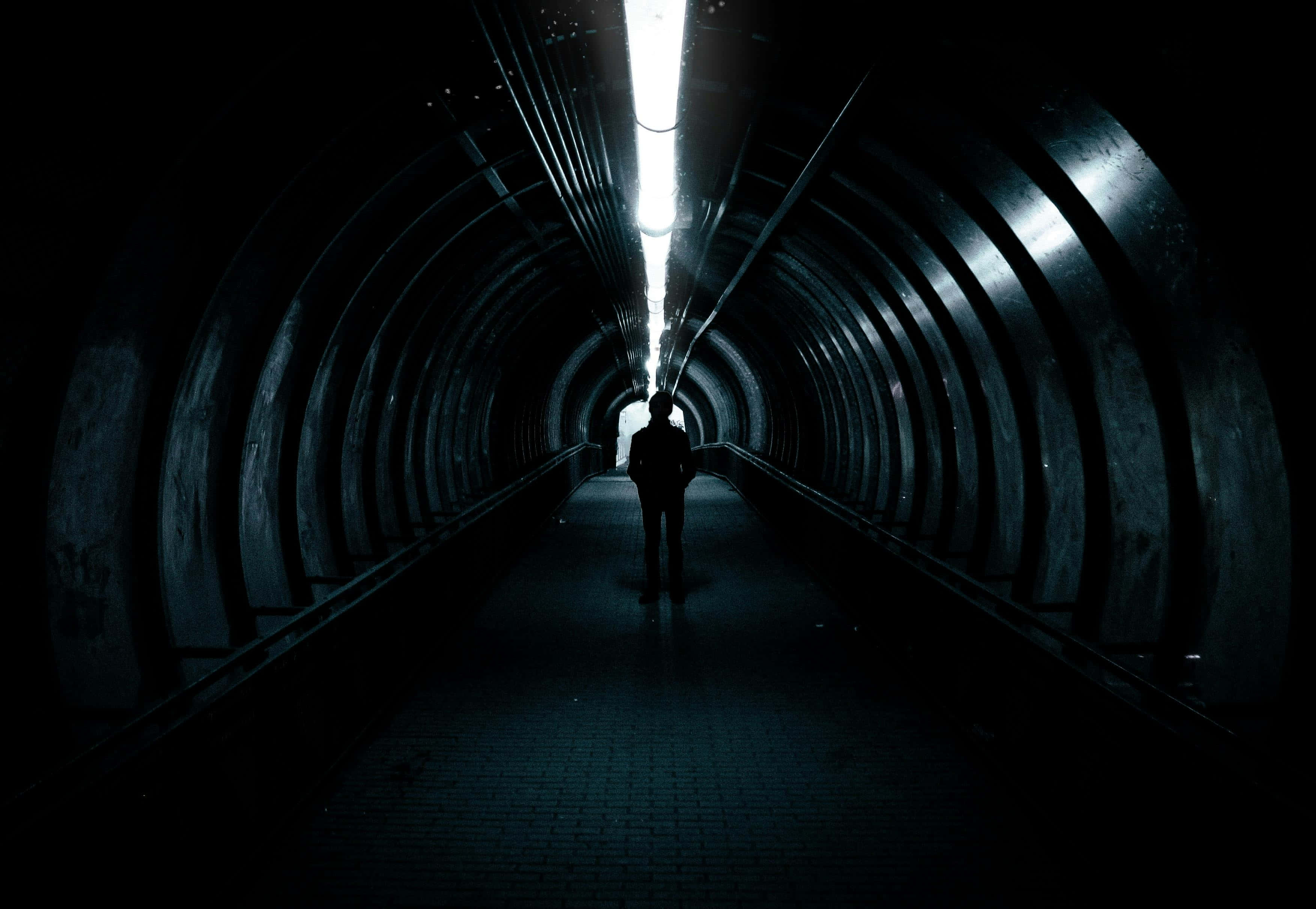 dark curved tunnel, overhead fluorescent light, lone silhouette, 2K Desktop Wallpaper