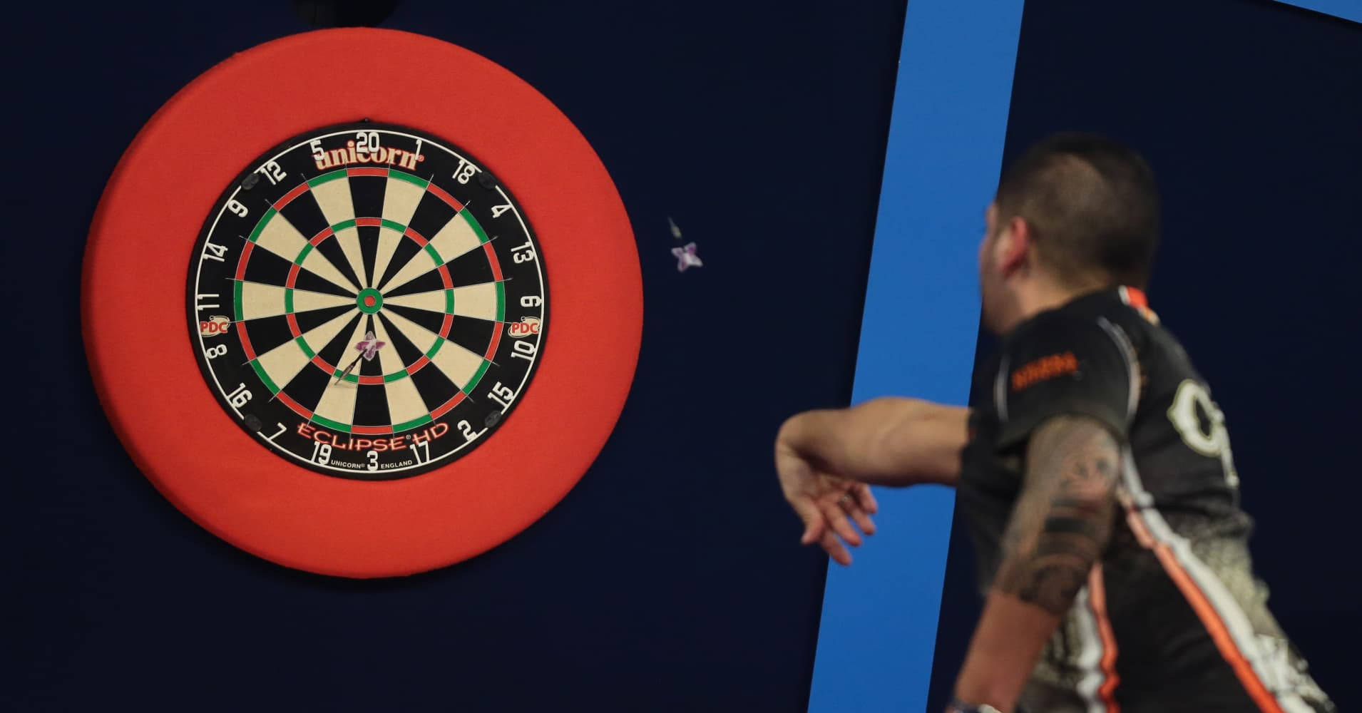 professional sport game darts athlete, red-framed dartboard, dimly lit competition setting, HD Desktop Wallpaper