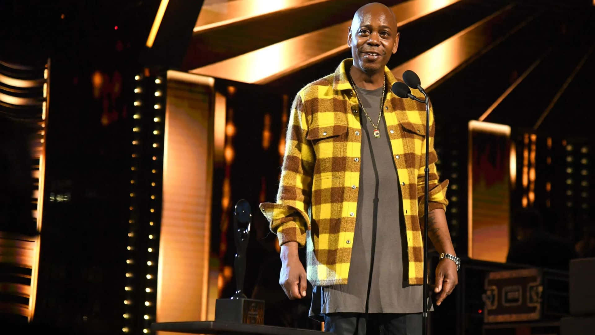 Dave Chappelle, yellow plaid shirt, warmly lit stage, Full HD Desktop Wallpaper