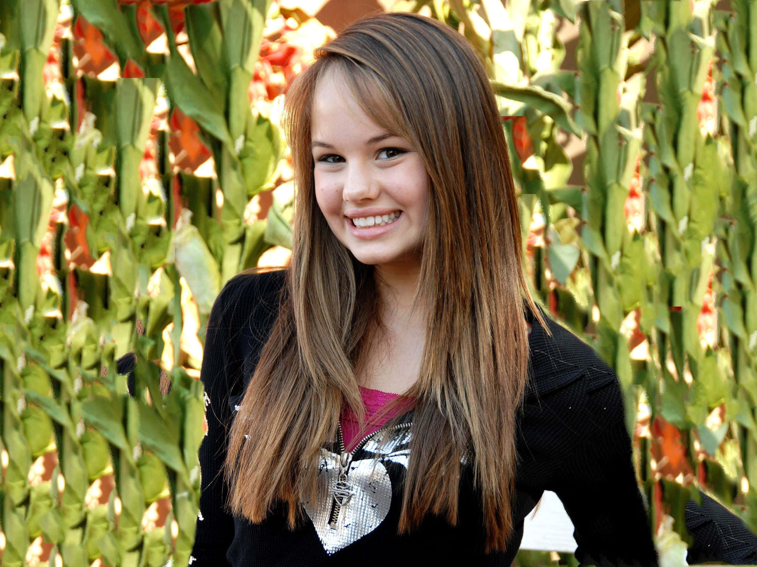 Debby Ryan, vibrant green leafy wall, warm sunlight, 2K Desktop Wallpaper