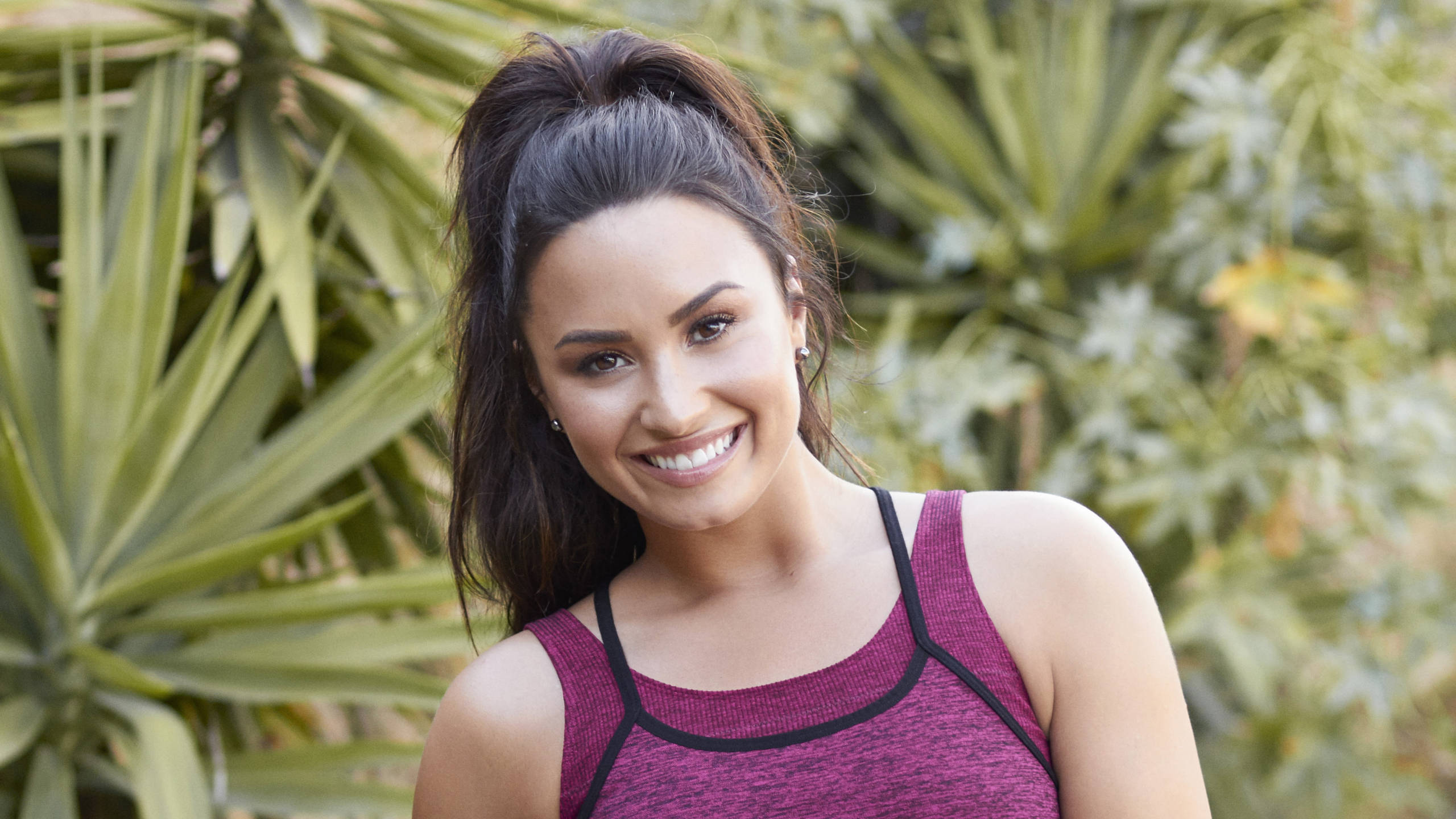 Demi Lovato, maroon athletic top, lush green foliage, 2K Desktop Wallpaper