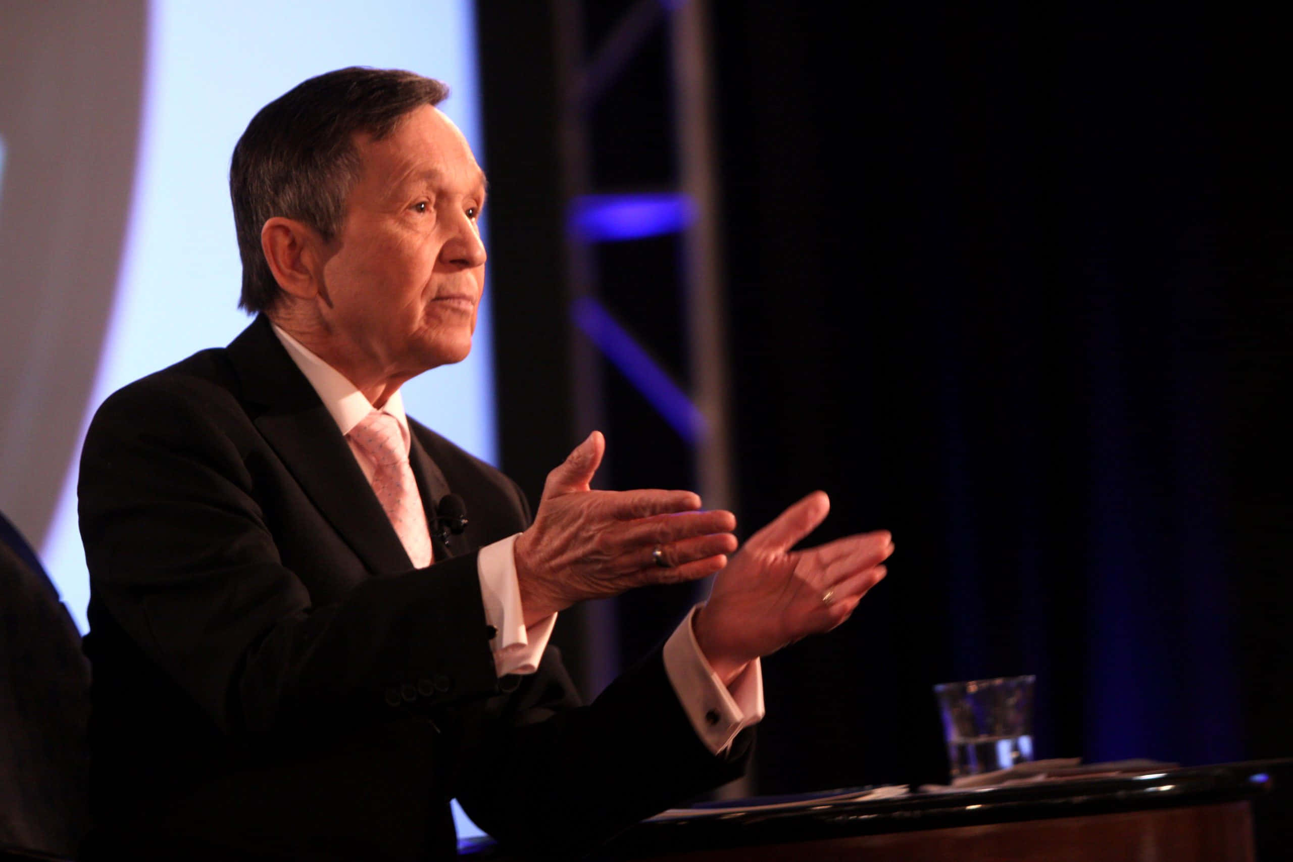 Dennis Kucinich, black suit, dimly lit stage, 2K Desktop Wallpaper