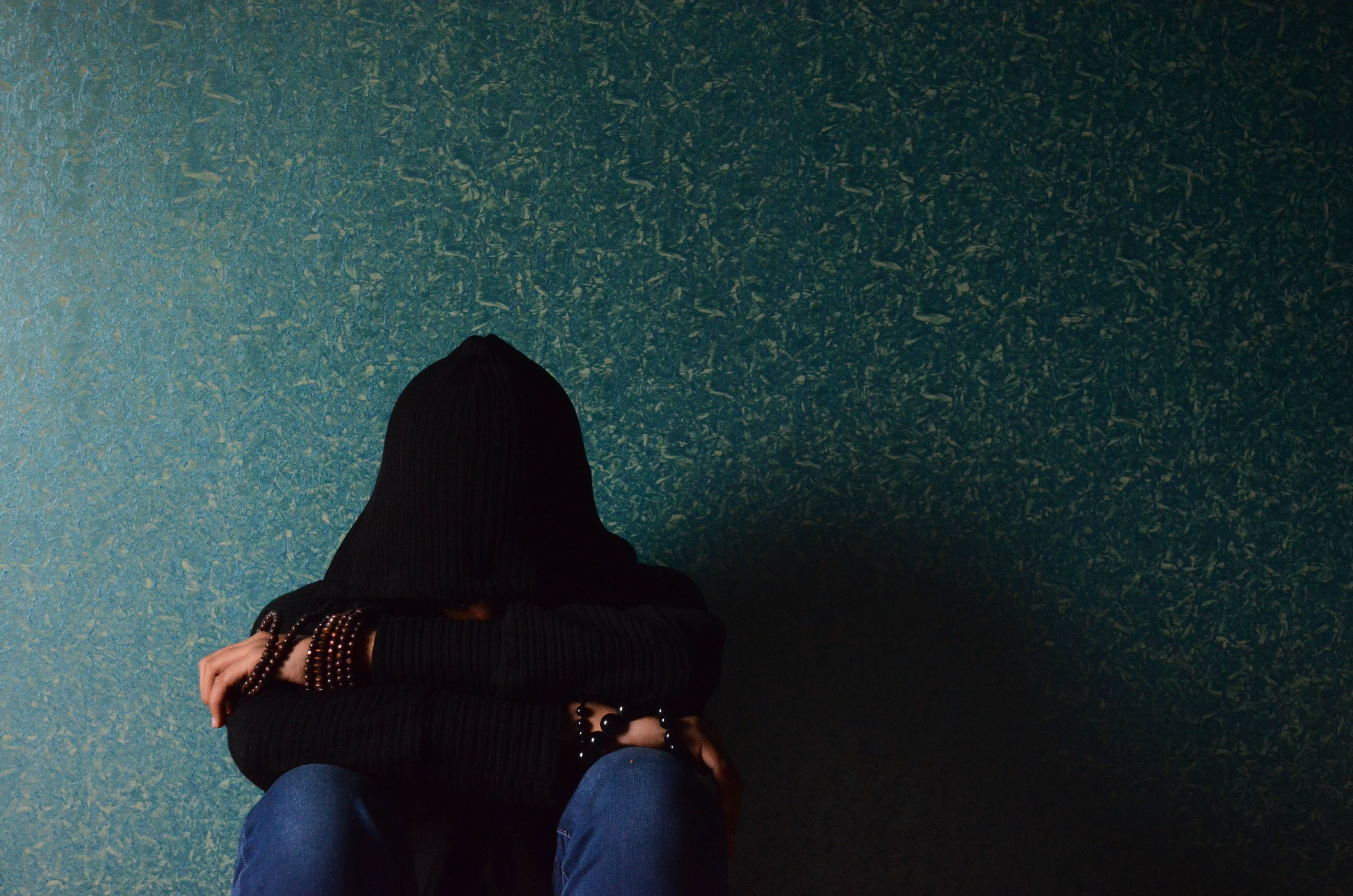 black hoodie, textured teal wall, hunched posture, 4K Desktop Wallpaper