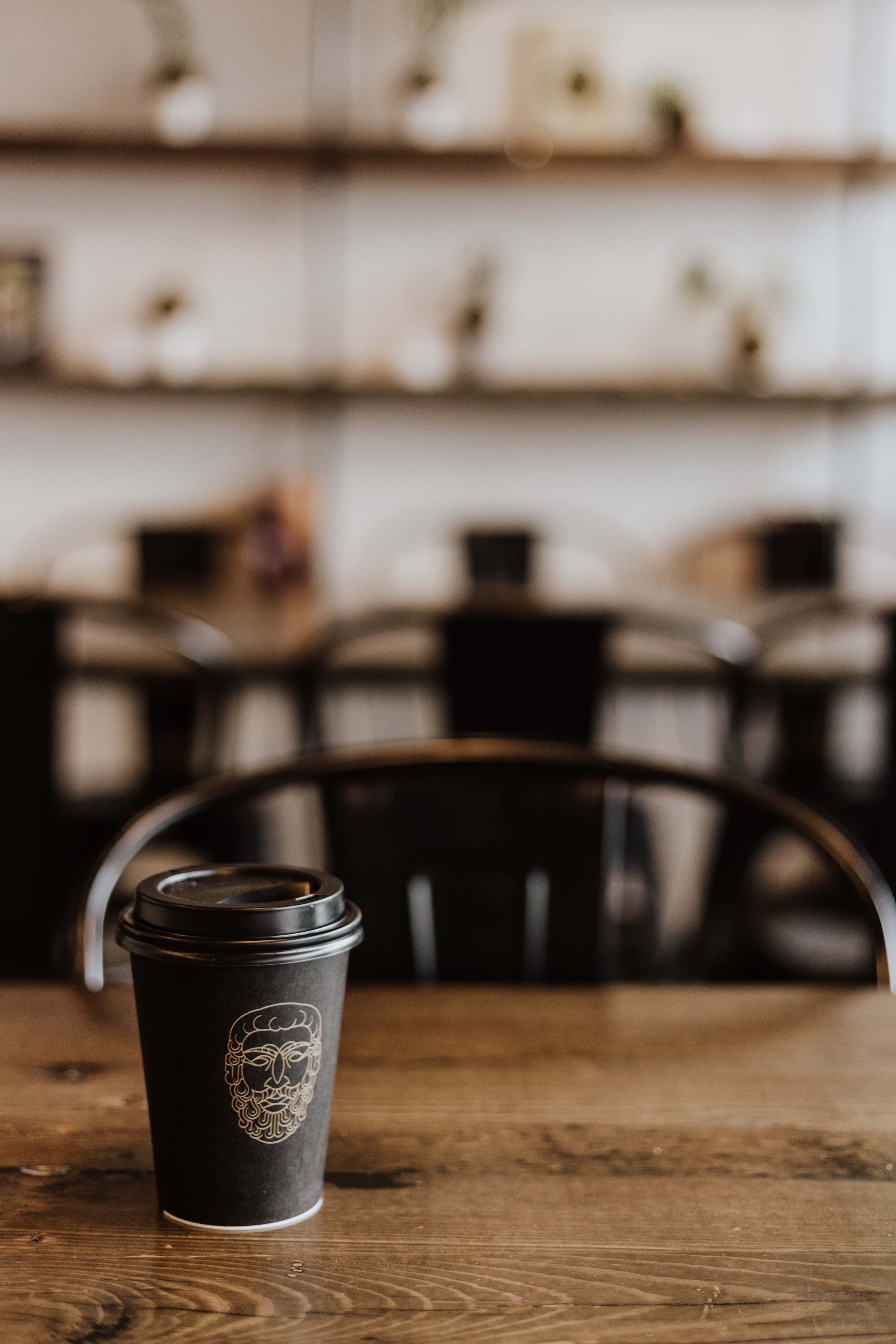 black disposable coffee cup, gold face logo, rustic wooden table, 5K Phone Wallpaper