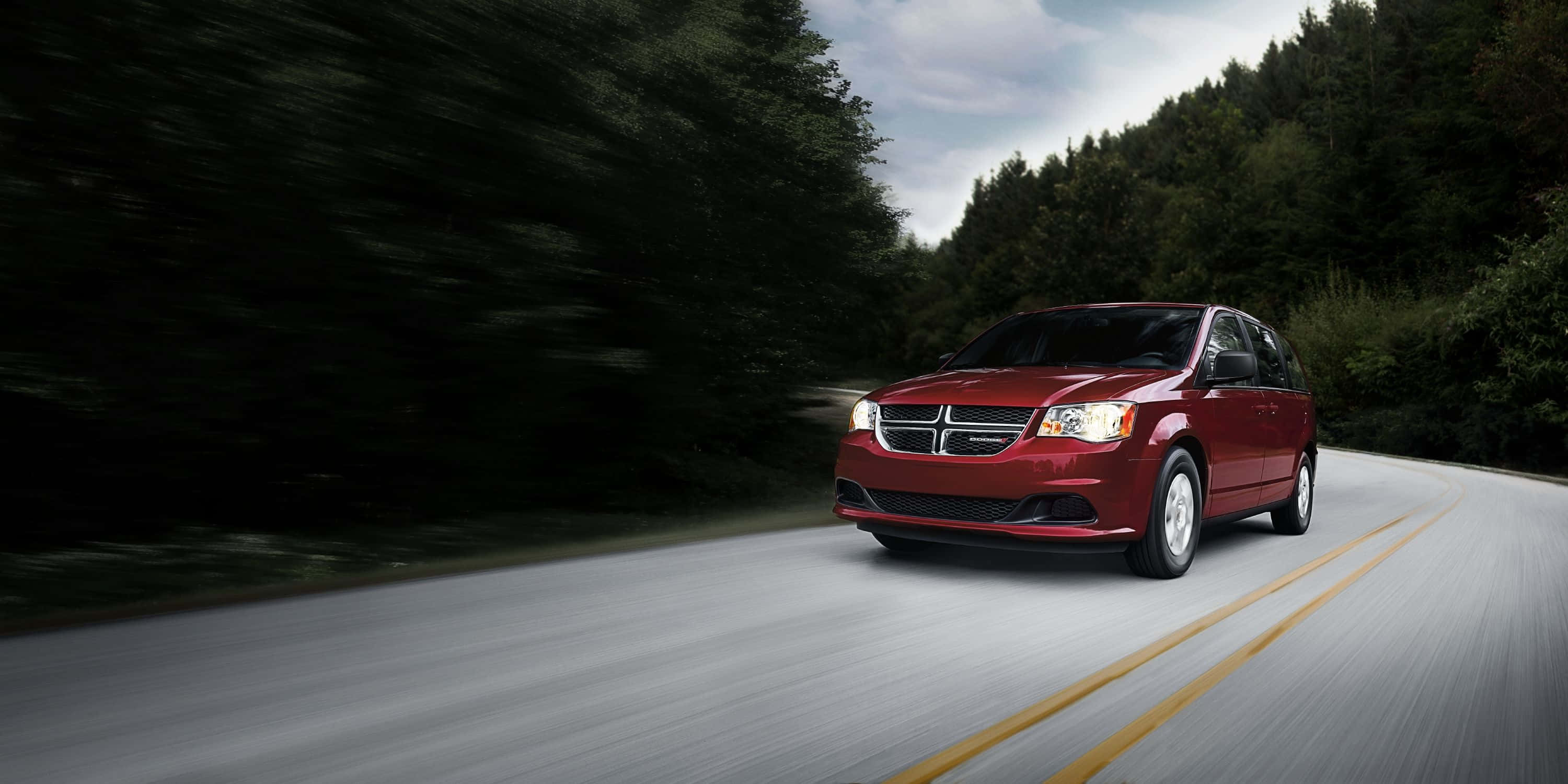 Red Dodge Grand Caravan, winding road, dense green forest, 2K Desktop Wallpaper