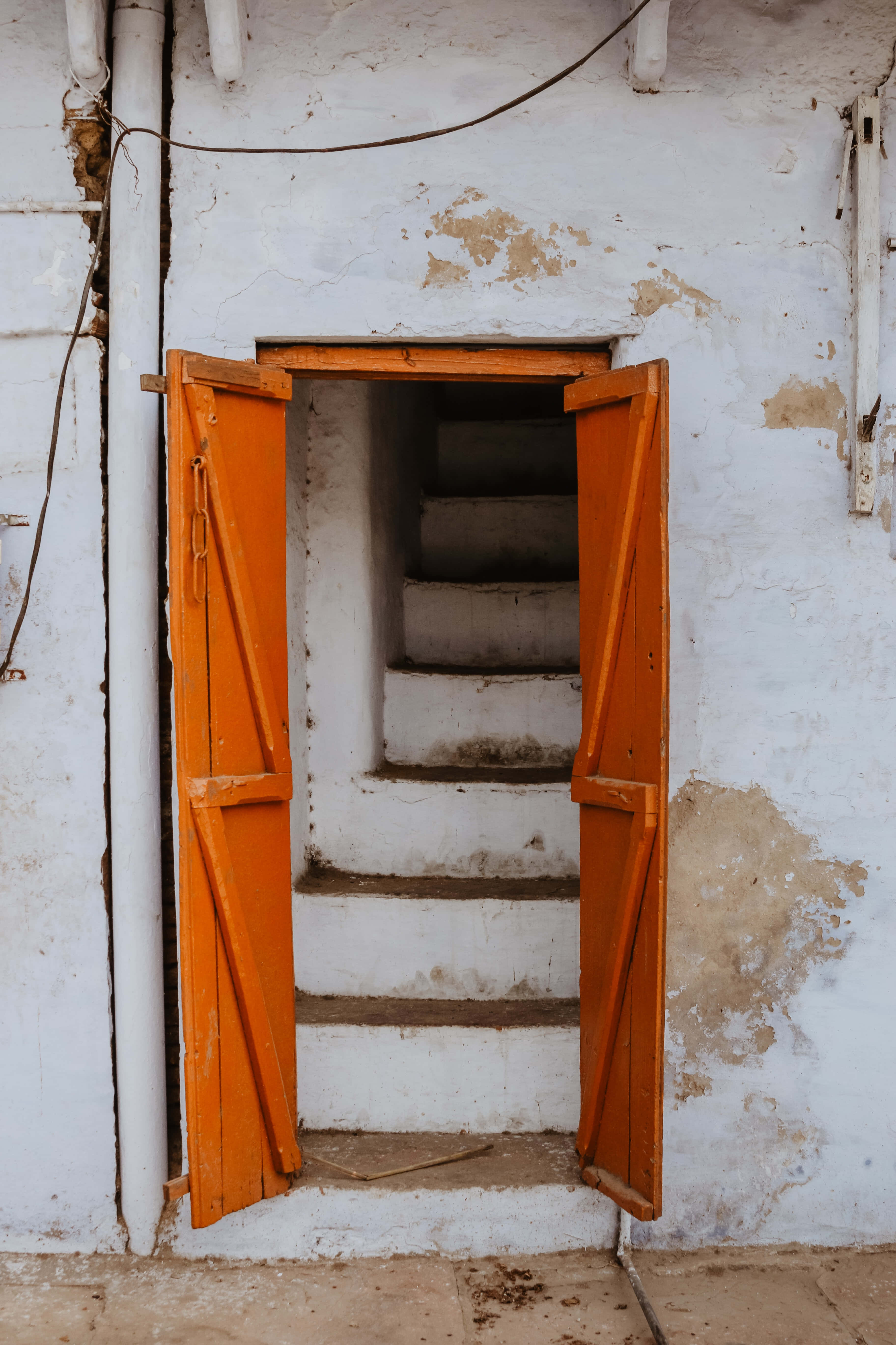 orange wooden door, narrow staircase, crumbling white-walled building, 5K Phone Wallpaper