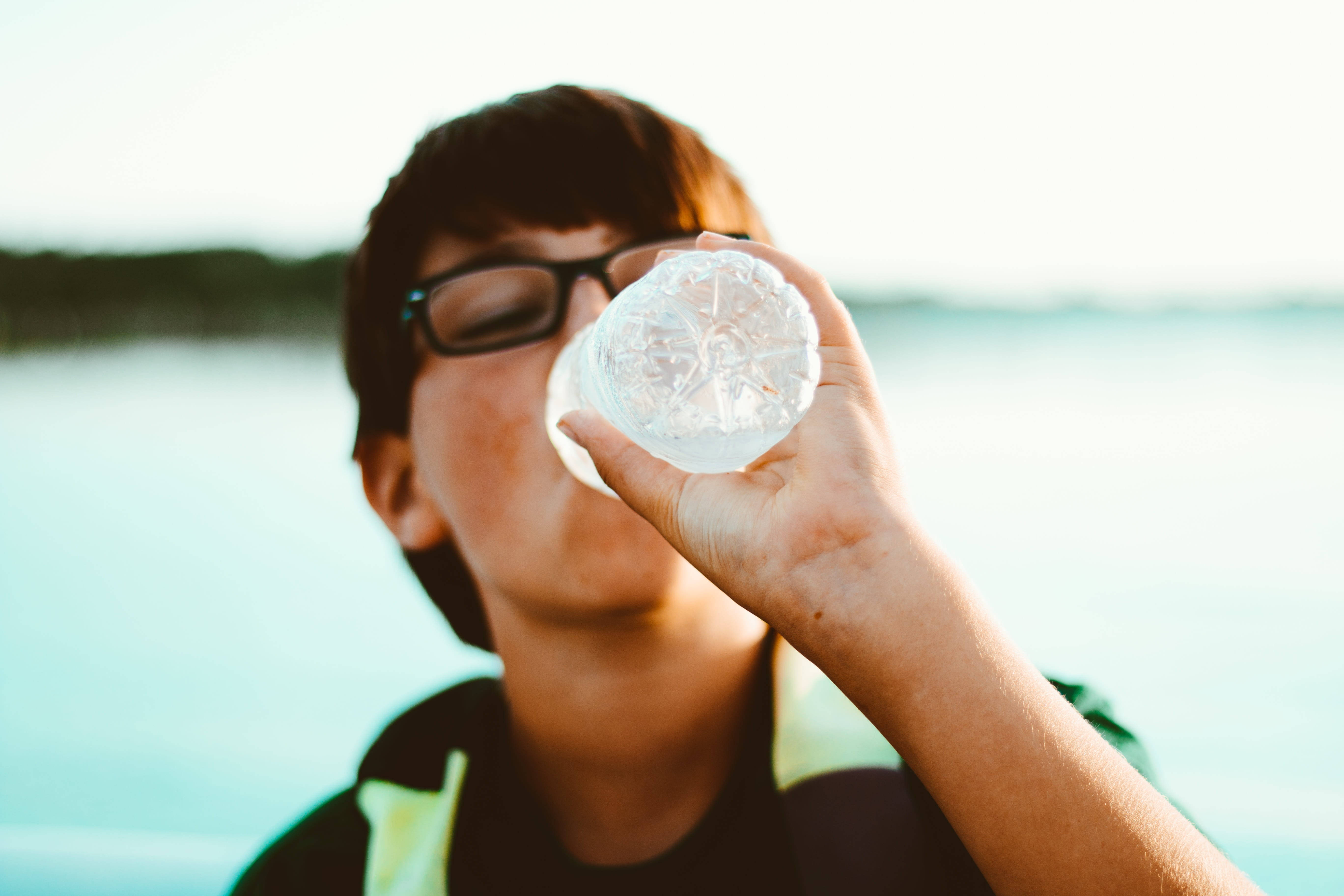 boy with glasses, clear plastic bottle, soft blurred lake backdrop, 5K Desktop Wallpaper