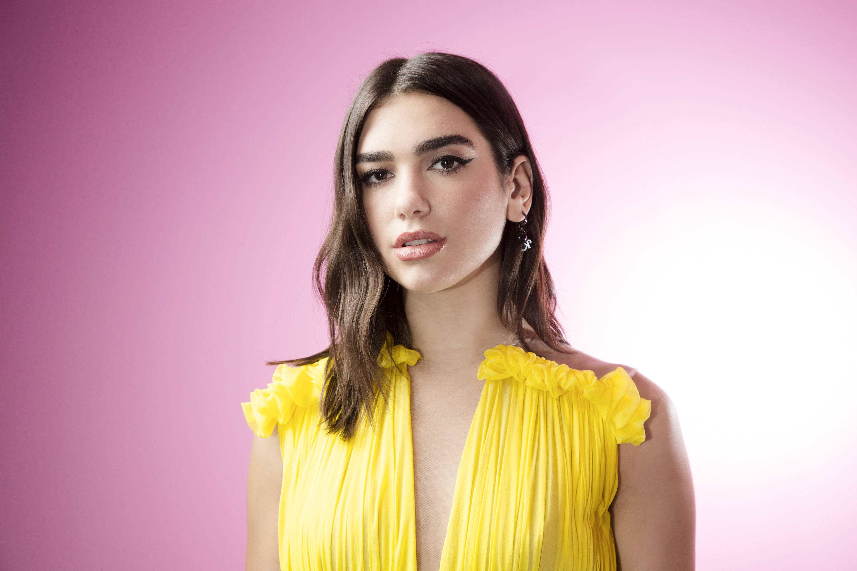 Dua Lipa, vibrant yellow ruffled top, soft pink gradient background, 2K Desktop Wallpaper