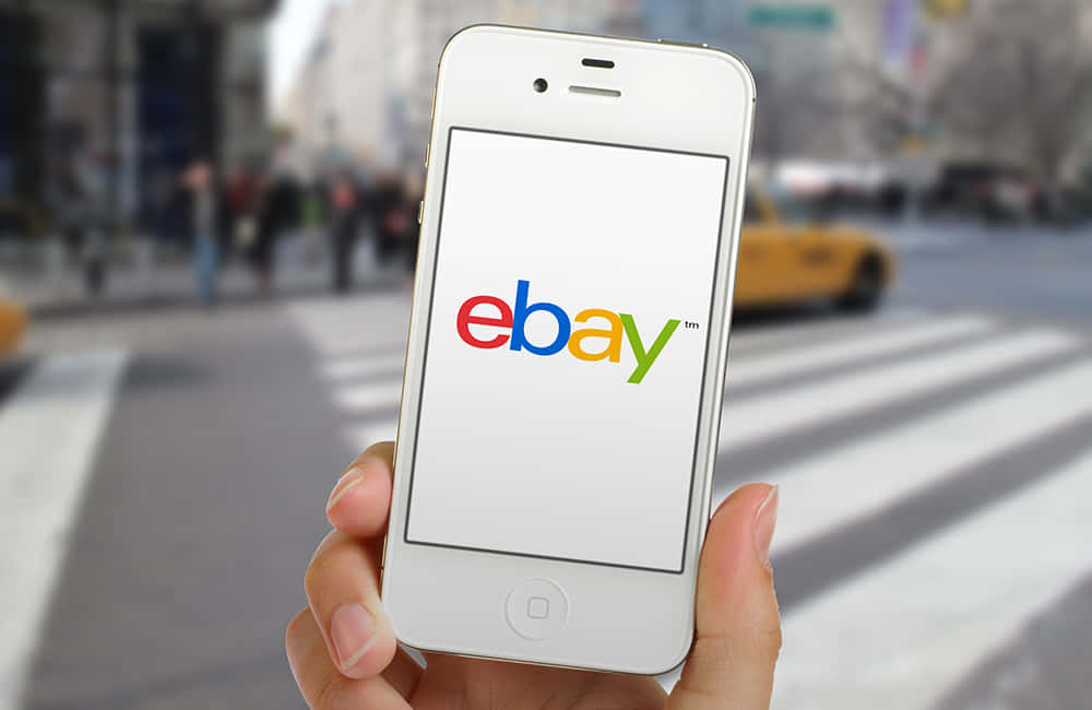 white iPhone, eBay UK logo, blurred city street, SD Desktop Wallpaper