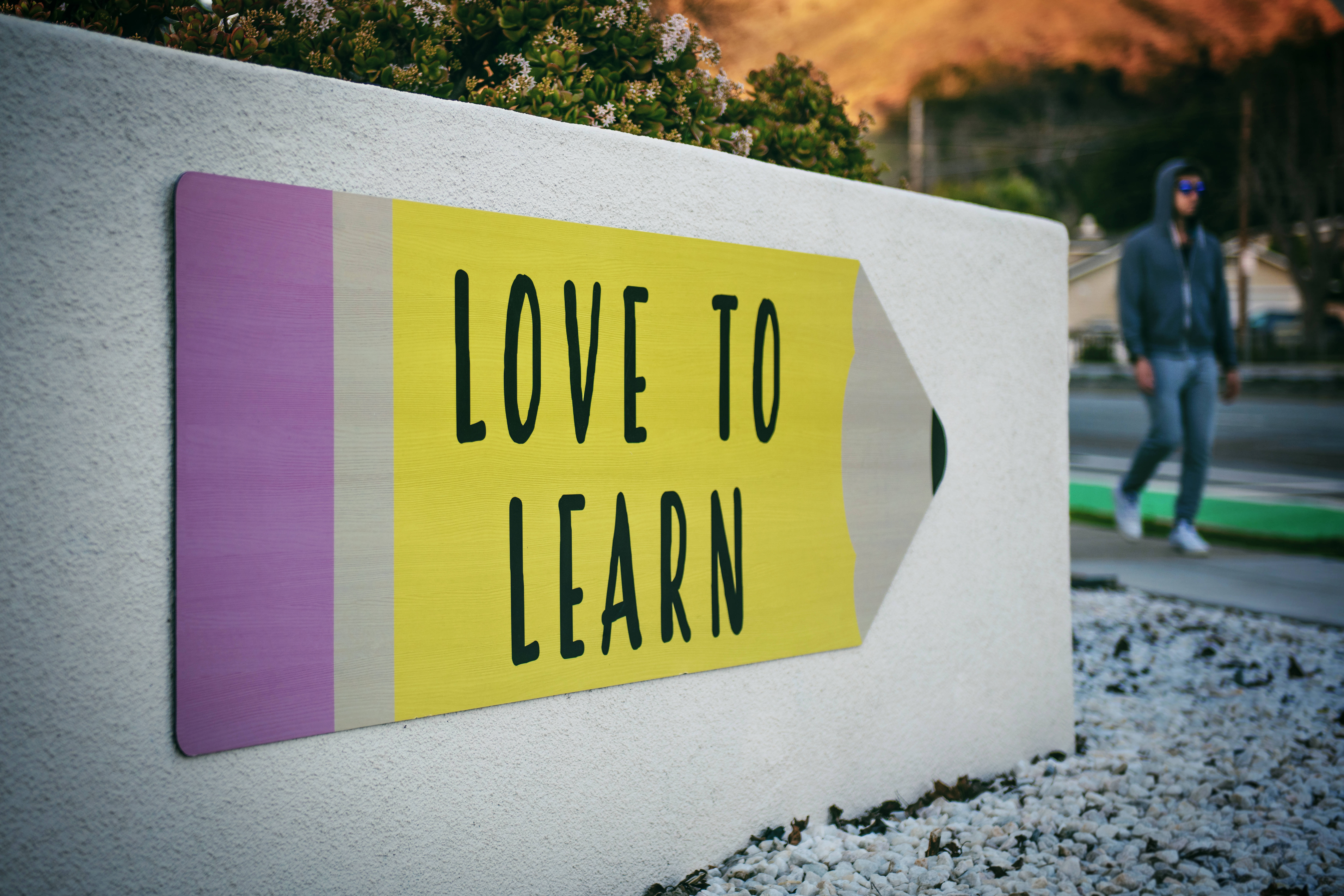 LOVE TO LEARN, vibrant yellow pencil-shaped sign, white wall, 8K Desktop Wallpaper