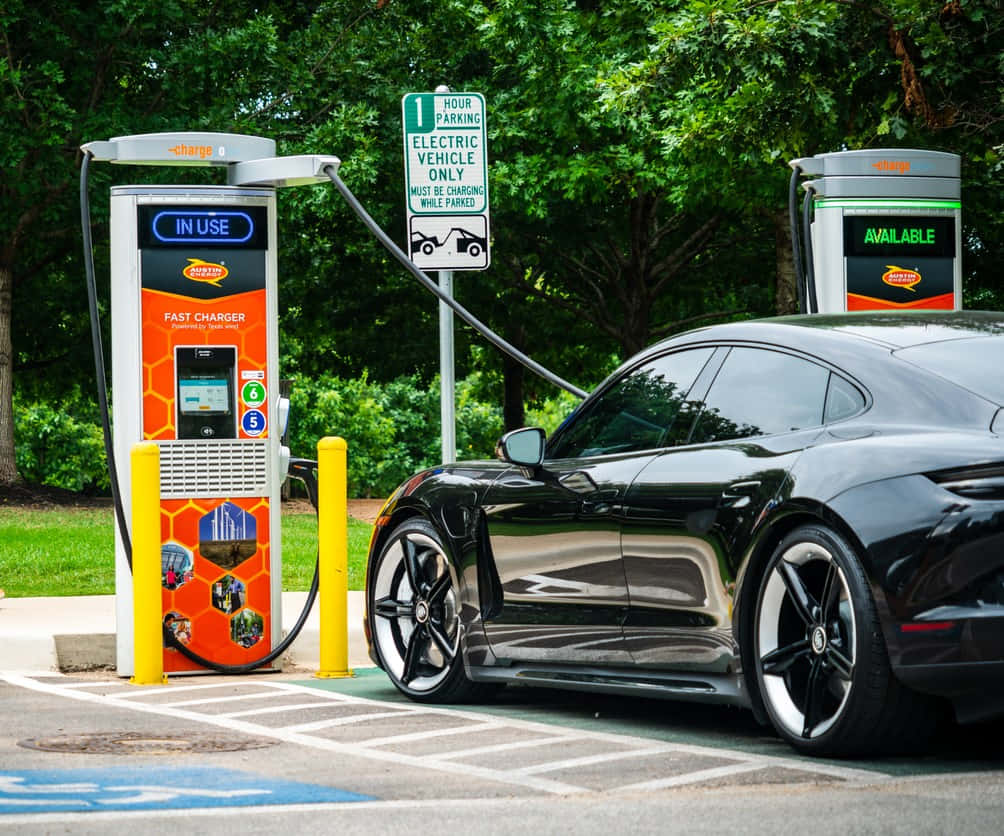 sleek black electric car, bright orange station, leafy green trees, SD Desktop Wallpaper