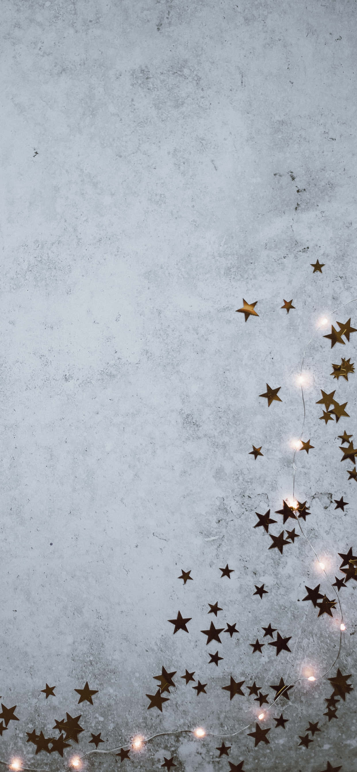 Golden star-shaped lights, textured gray concrete wall, festive display, 2K Phone Wallpaper
