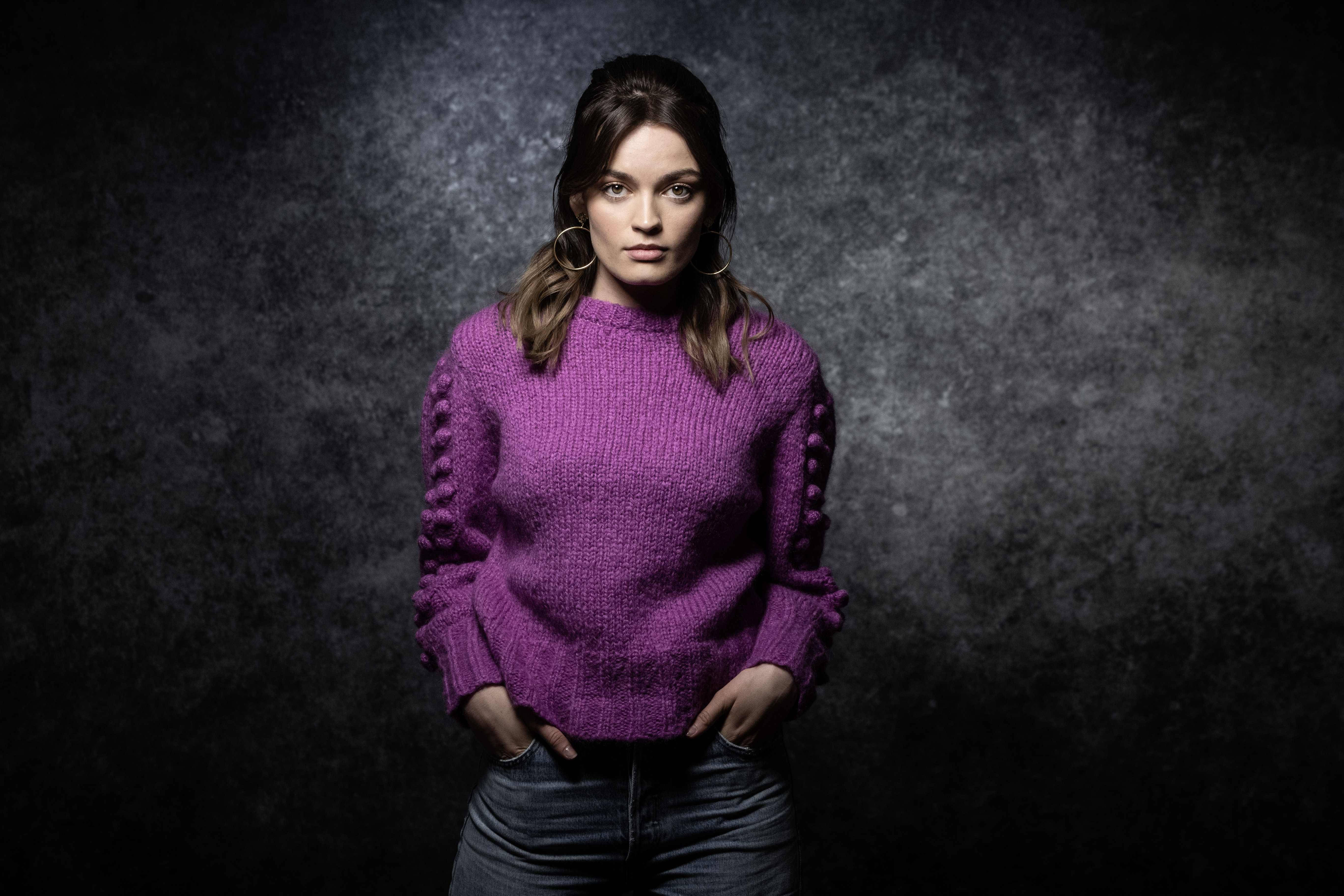 Emma Mackey, vibrant purple knit sweater, dark textured studio backdrop, 5K Desktop Wallpaper